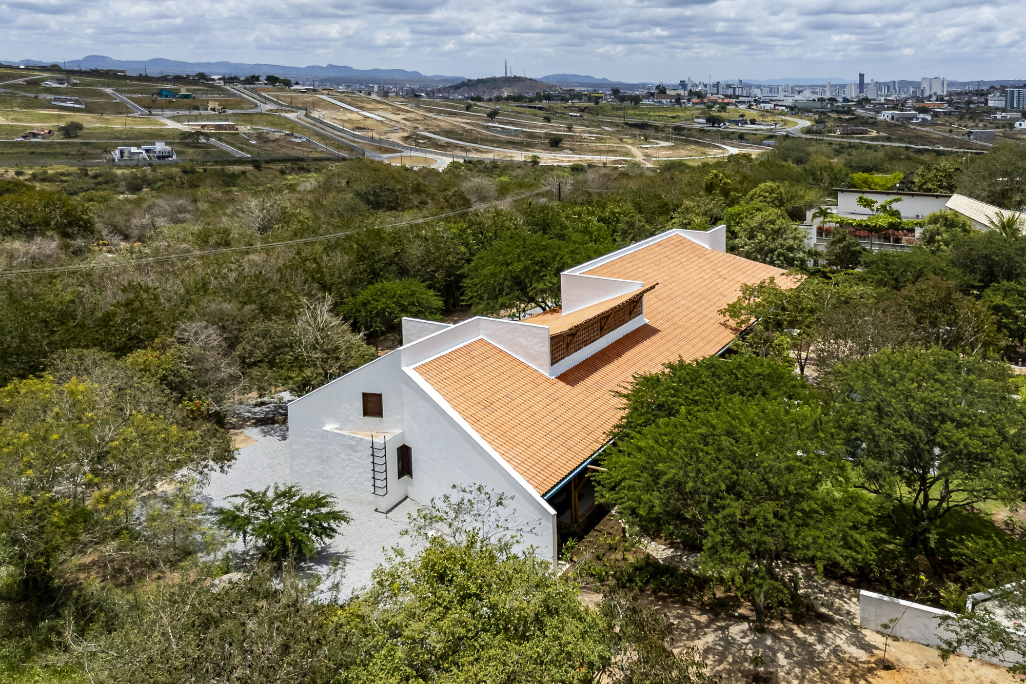 Elevated view of the terracotta tiled roof with protruding clerestory volume nestled among green trees
