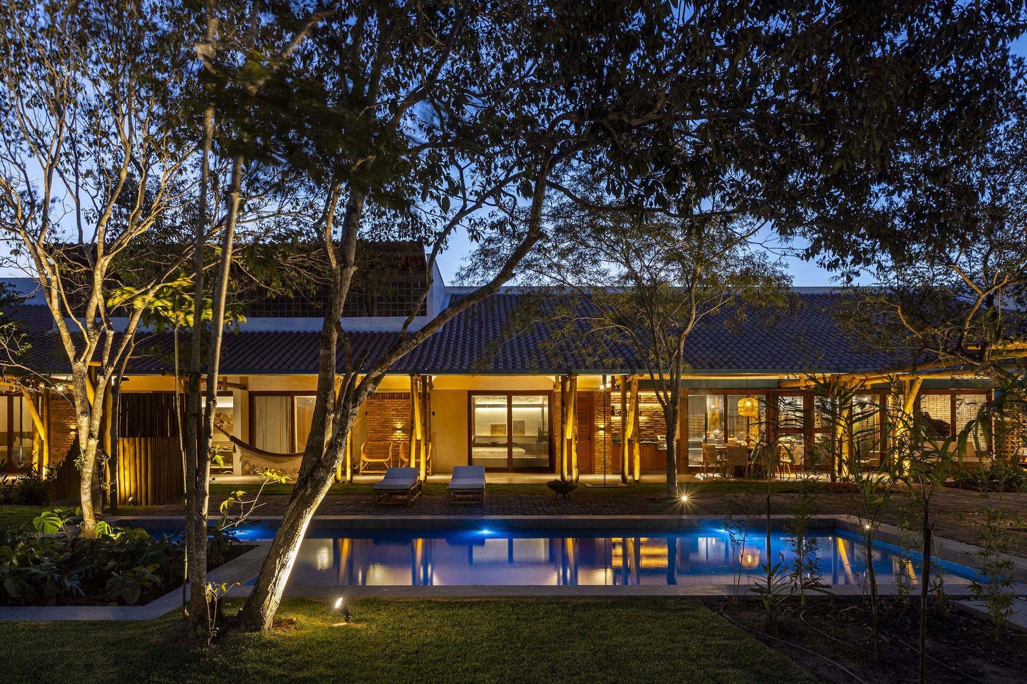 Courtyard view of tiled roof residence with pool and uplighting among trees at evening