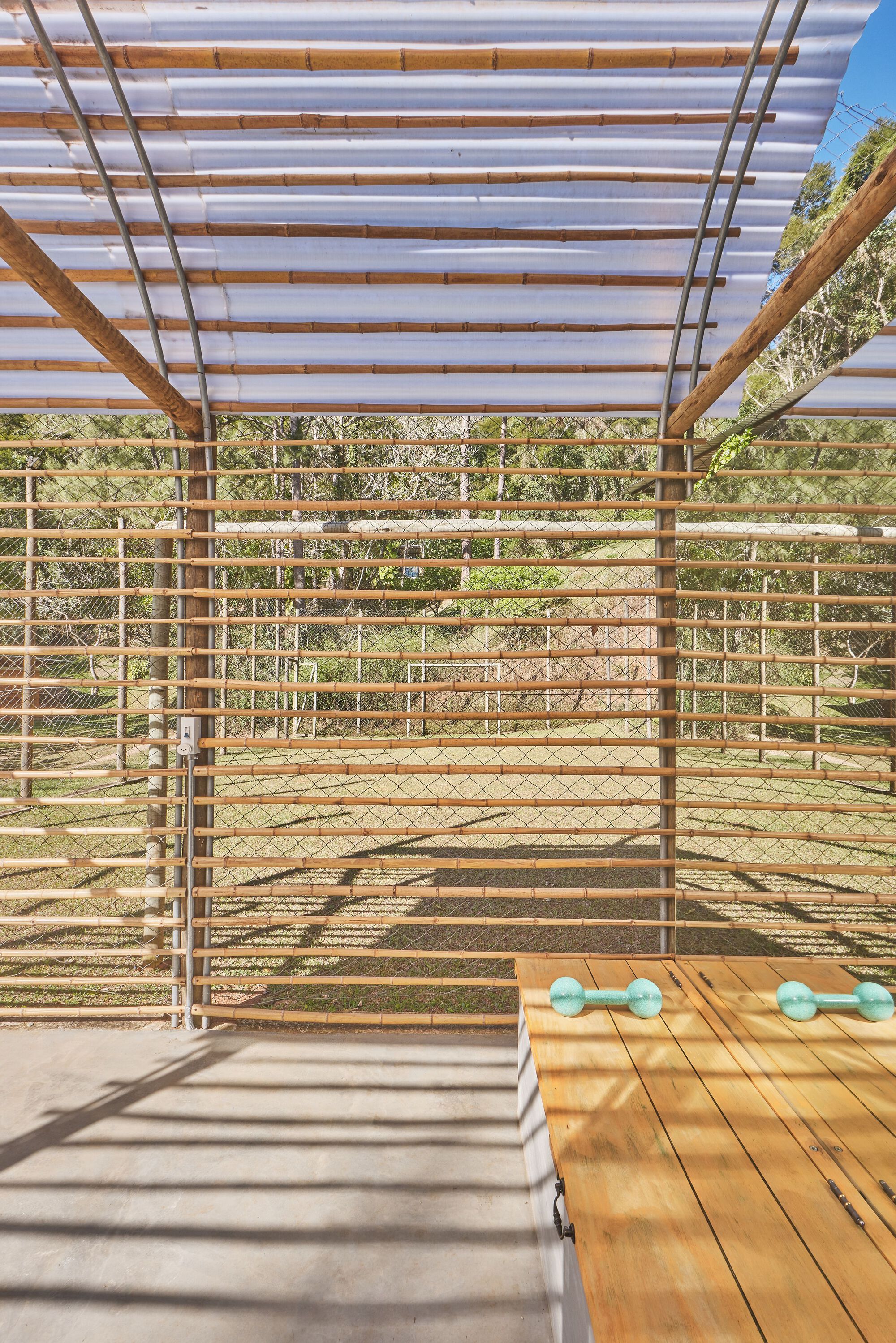 View toward the landscape through horizontal timber slats with corrugated canopy above casting striped shadows