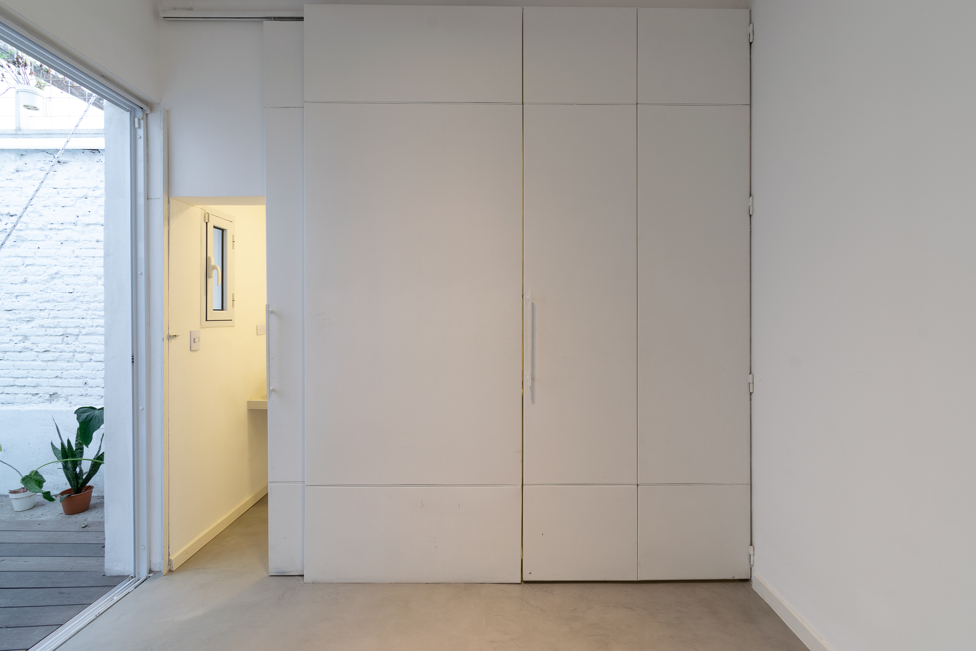 Floor-to-ceiling paneled storage wall with concealed door opening to a yellow-lit passageway