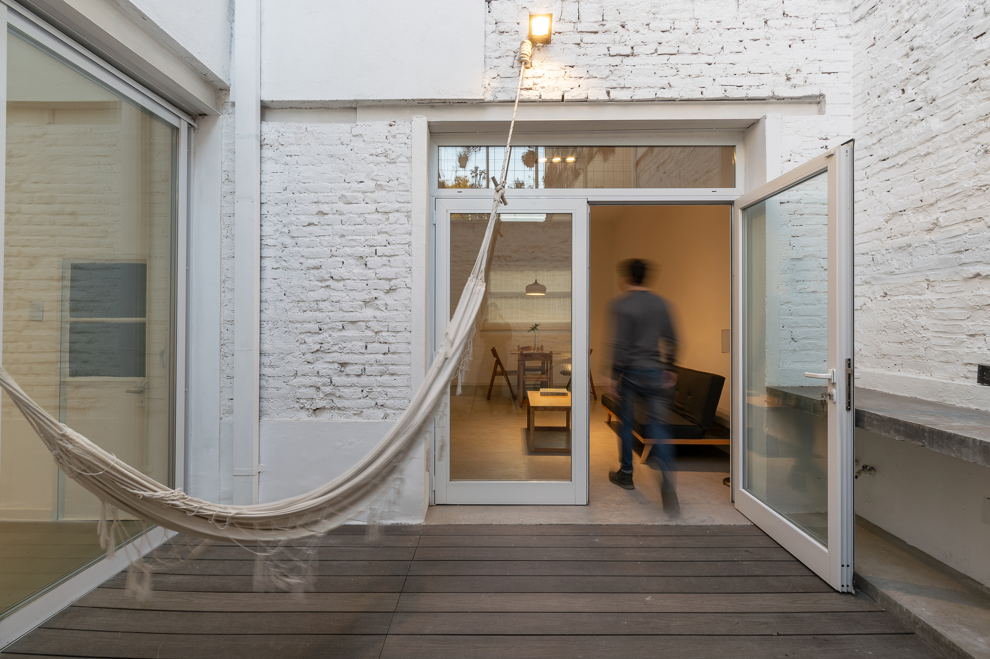 Glazed door opening onto timber deck courtyard with hammock and a blurred walking figure