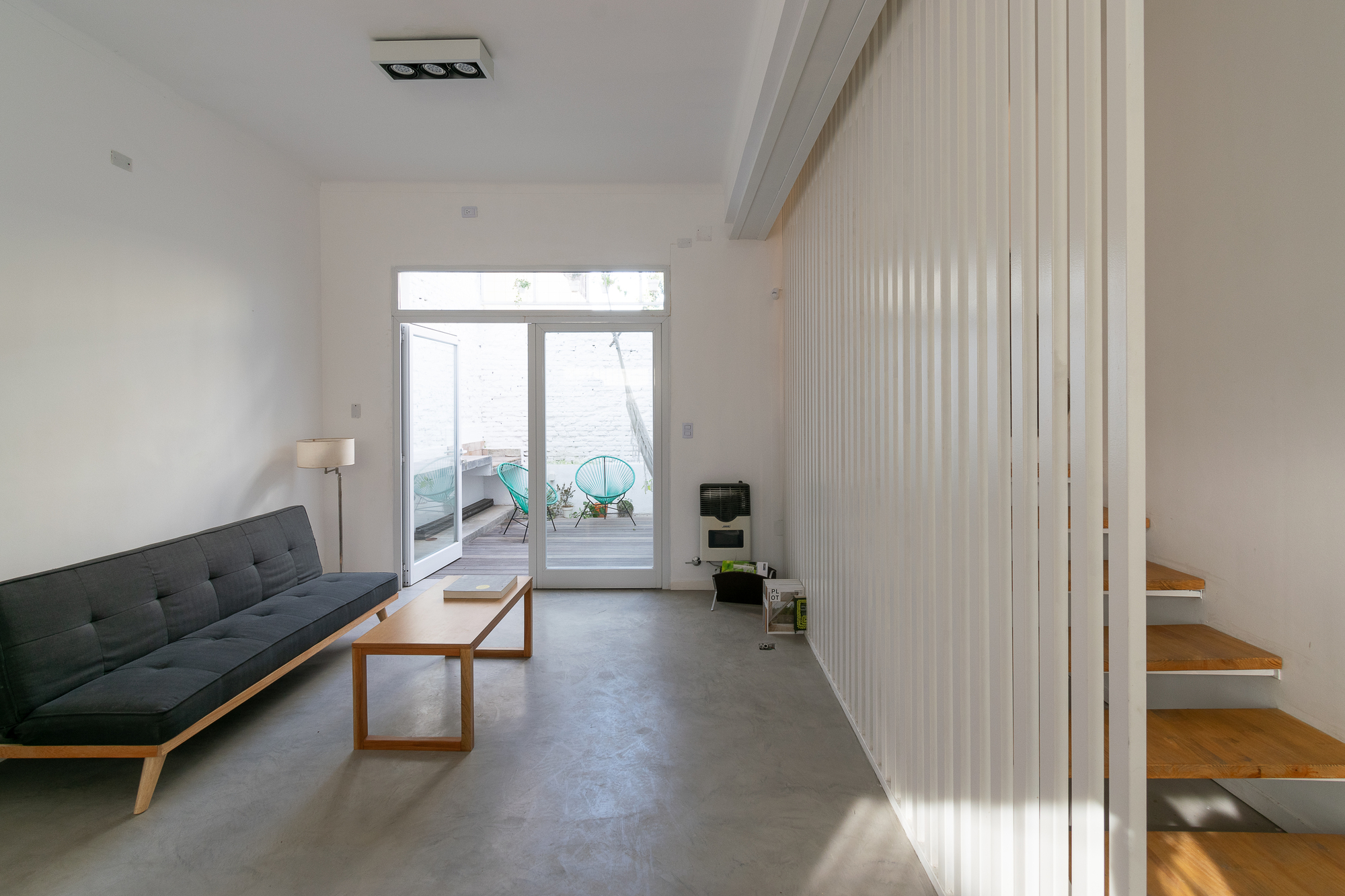 Living space with concrete floor and vertical screen adjacent to cantilevered timber stair treads