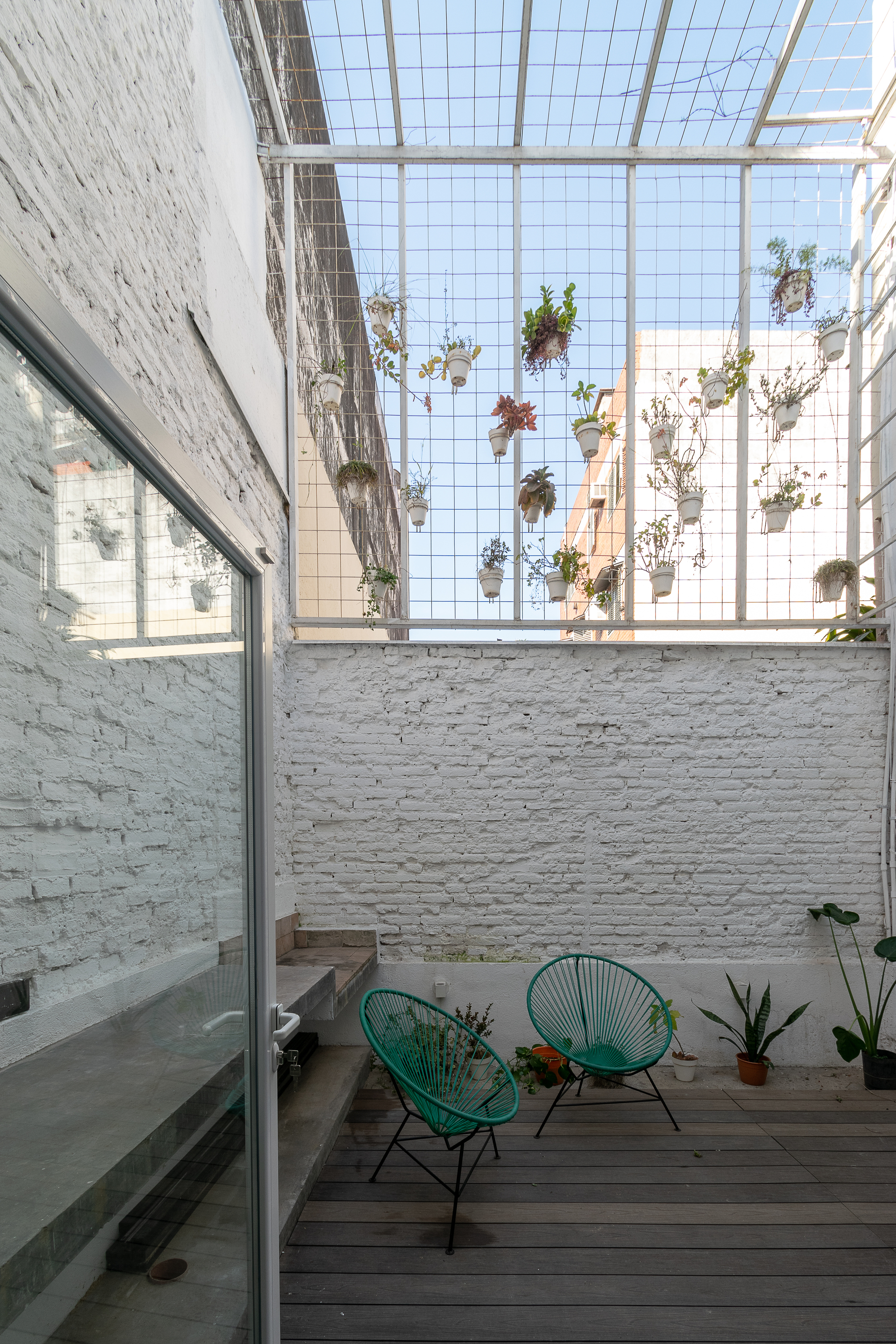 Courtyard with painted brick walls, timber deck and hanging planters suspended beneath wire mesh skylight