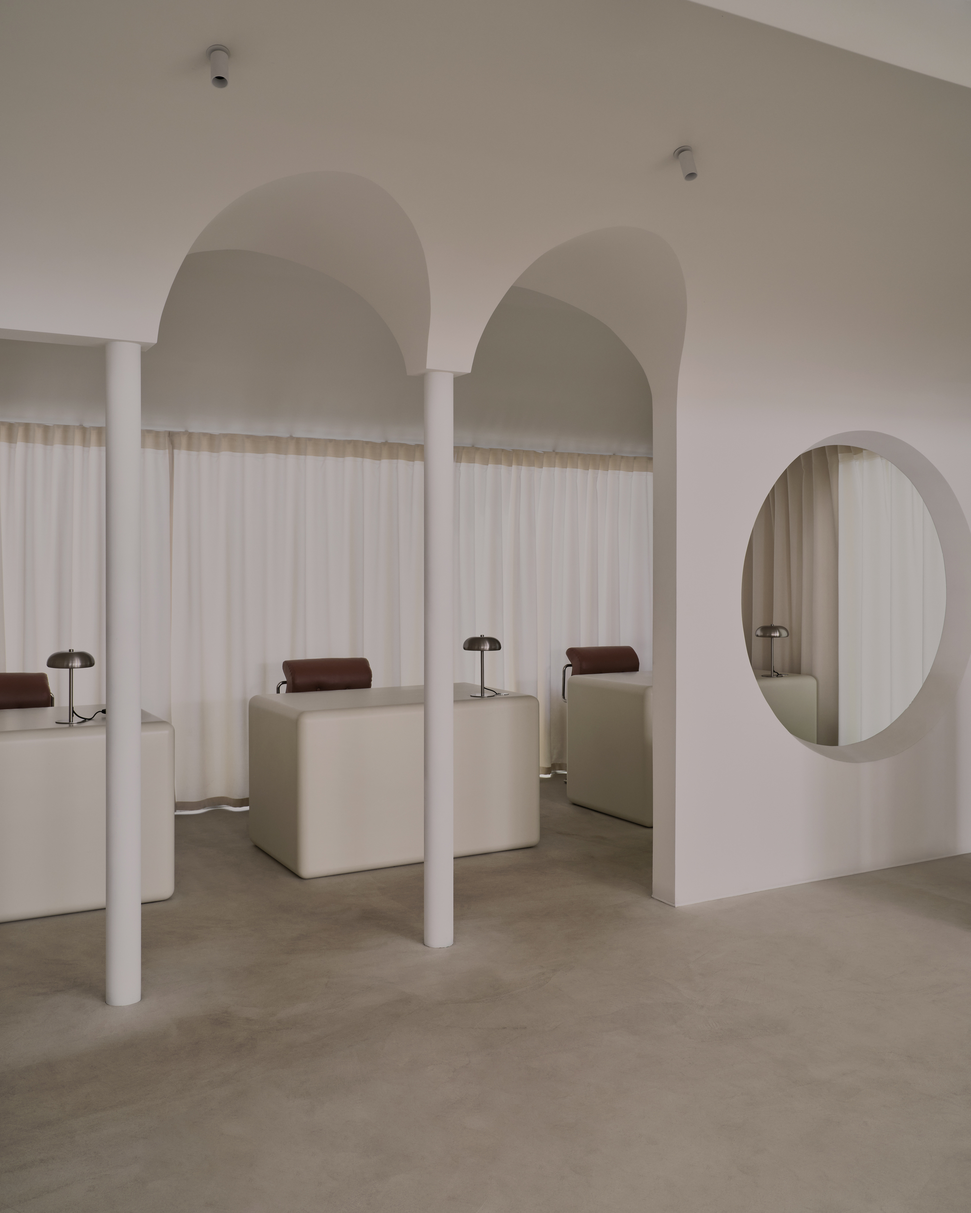 White cylindrical columns framing arched openings and a circular wall mirror under soft overhead lighting