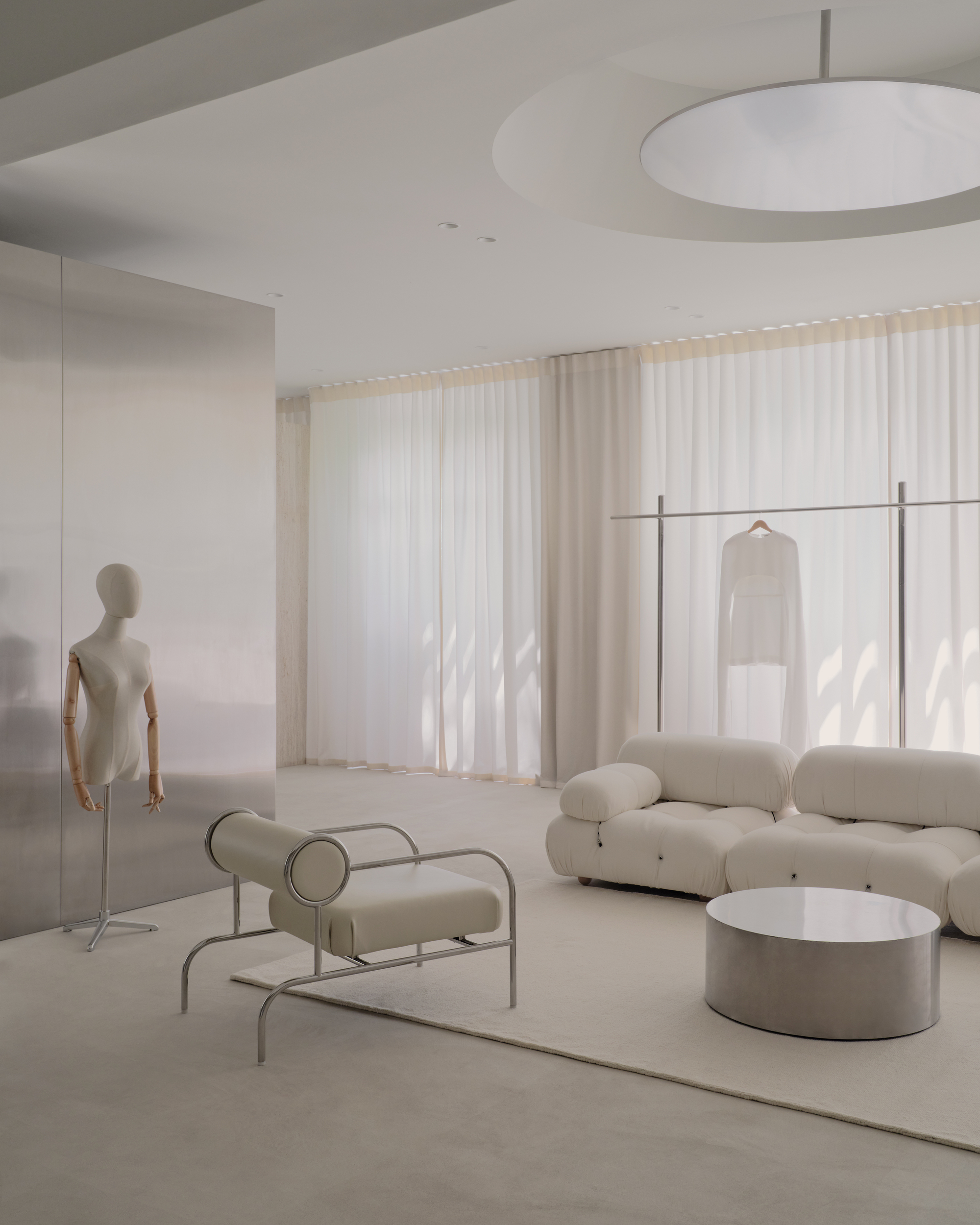 Retail interior with mannequin, tubular seating and sheer curtains filtering natural light from windows