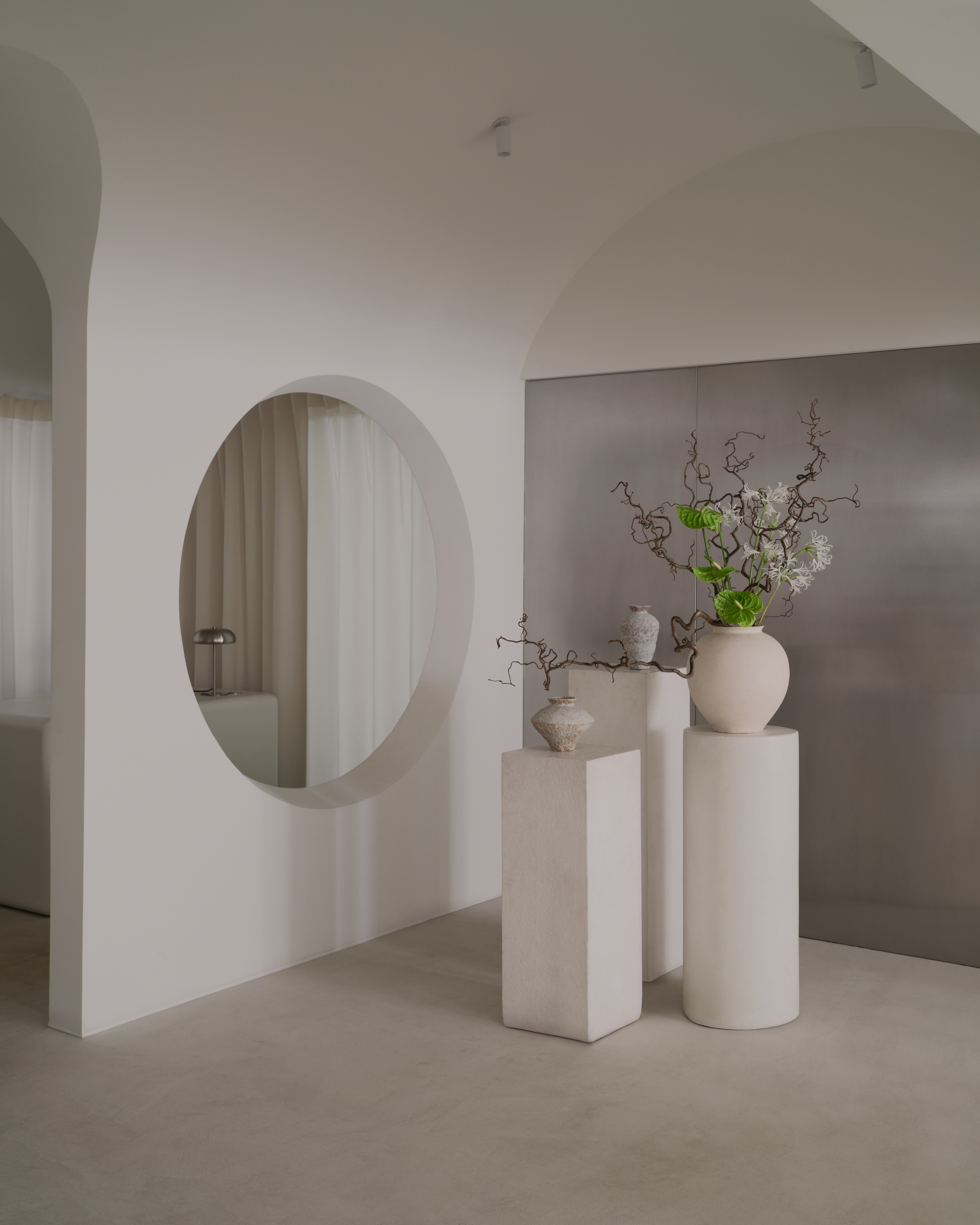 Circular aperture in white wall framing view of sheer curtains with ceramic vases on pedestals in foreground