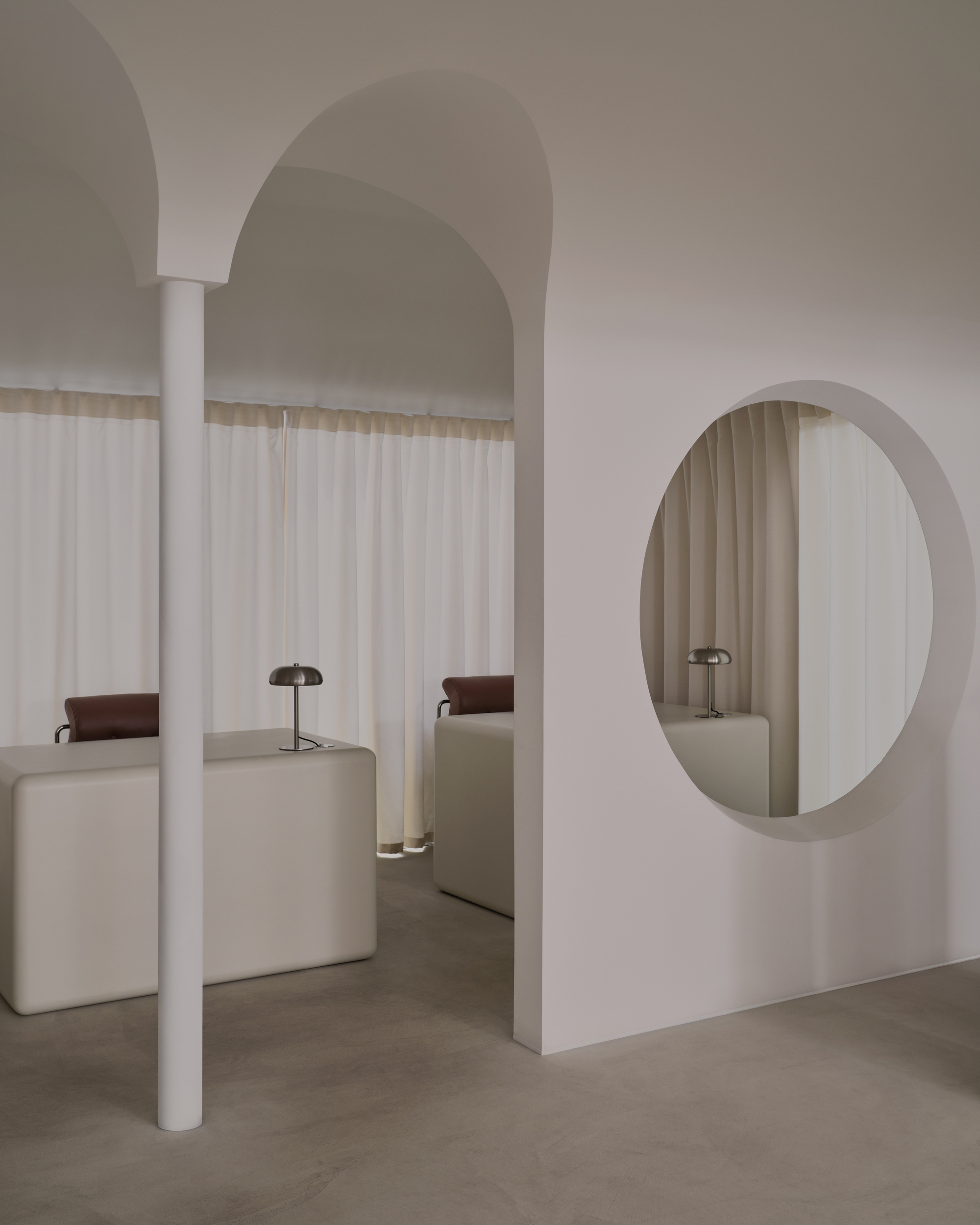 White cylindrical column supporting arched ceiling vault with oval mirror and arched alcoves in background