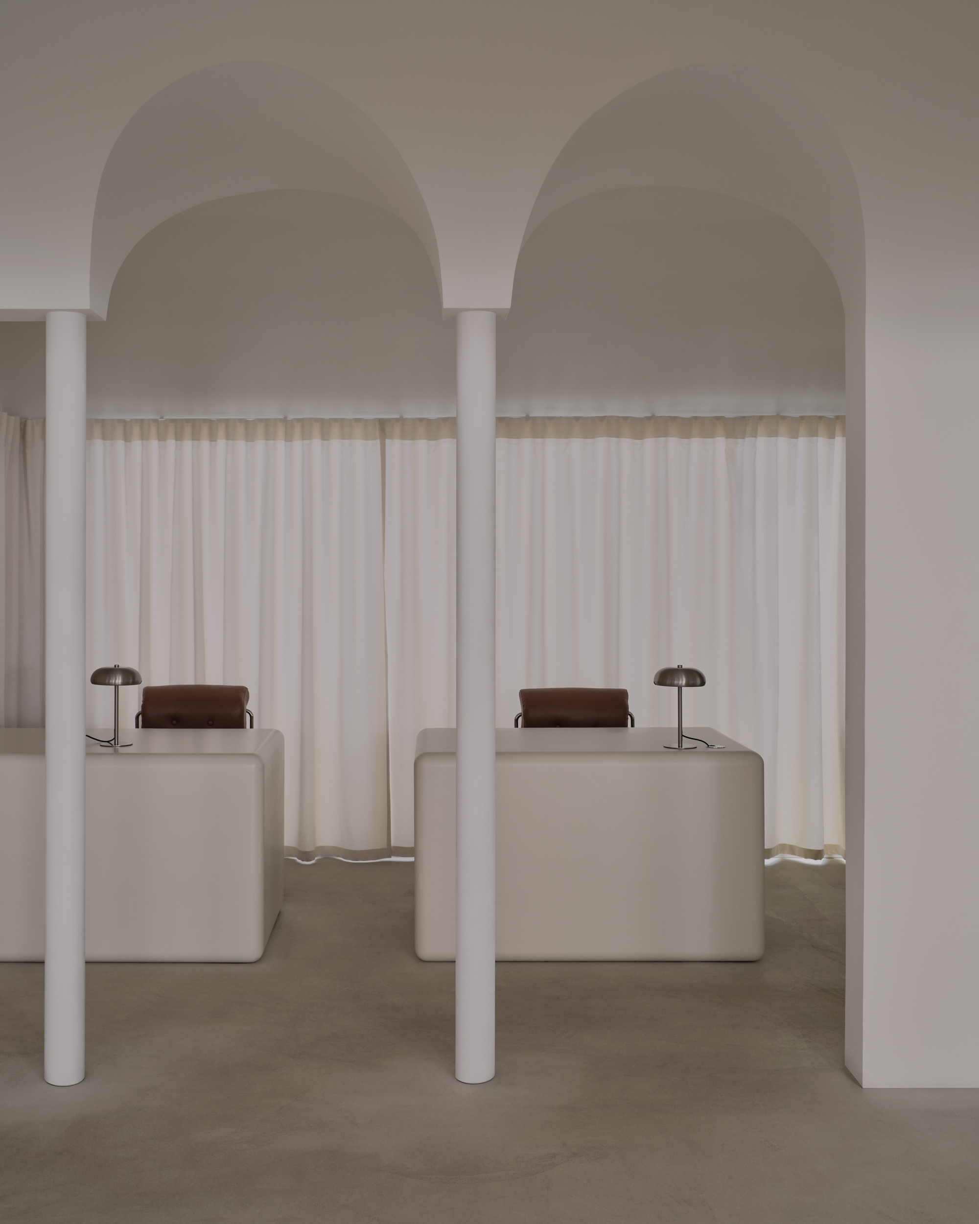 Symmetrical pair of arched alcoves with white columns, sheer curtains, and upholstered seating blocks with table lamps