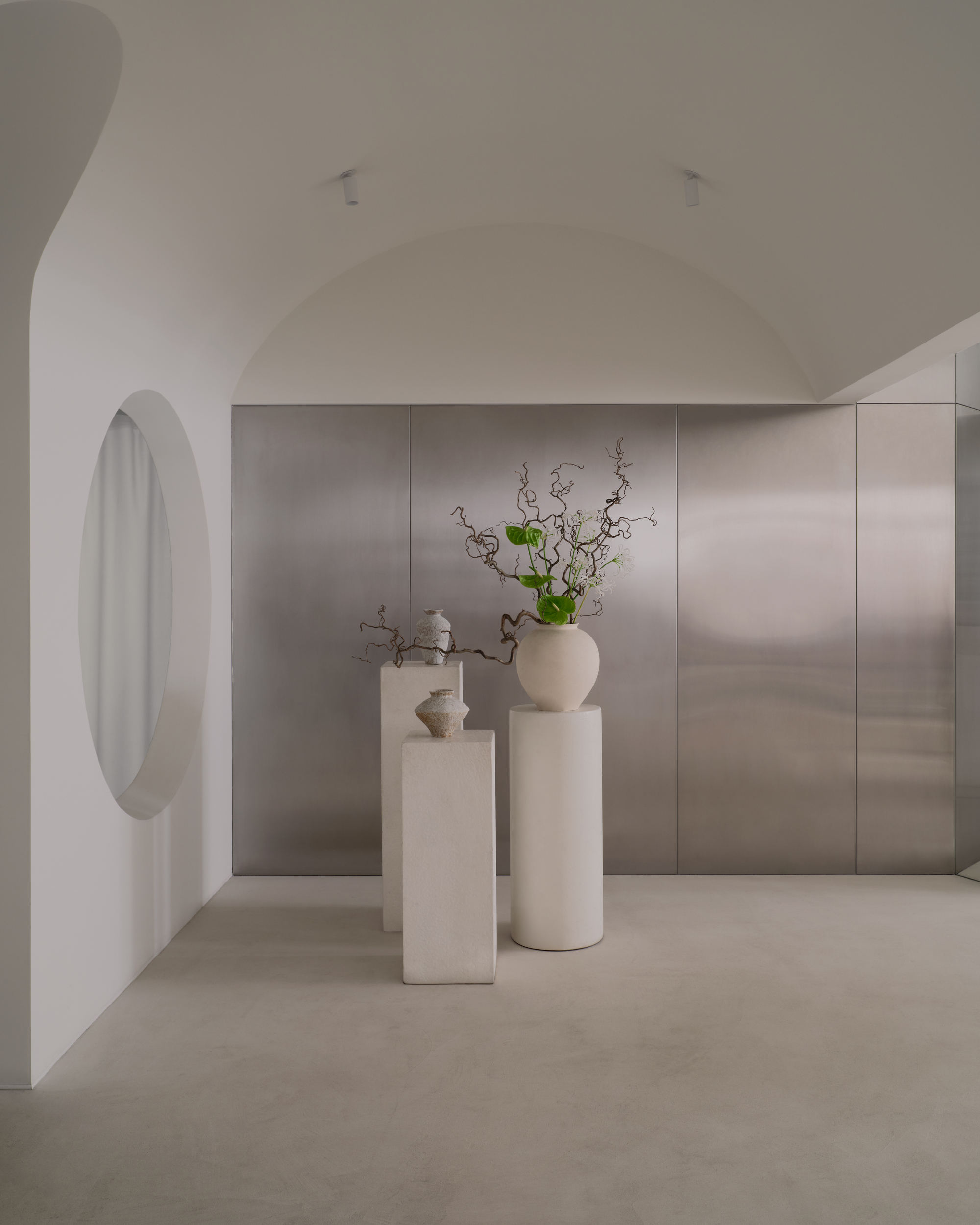Arched hallway with circular window opening onto stone-paneled wall and ceramic pedestals with green branches