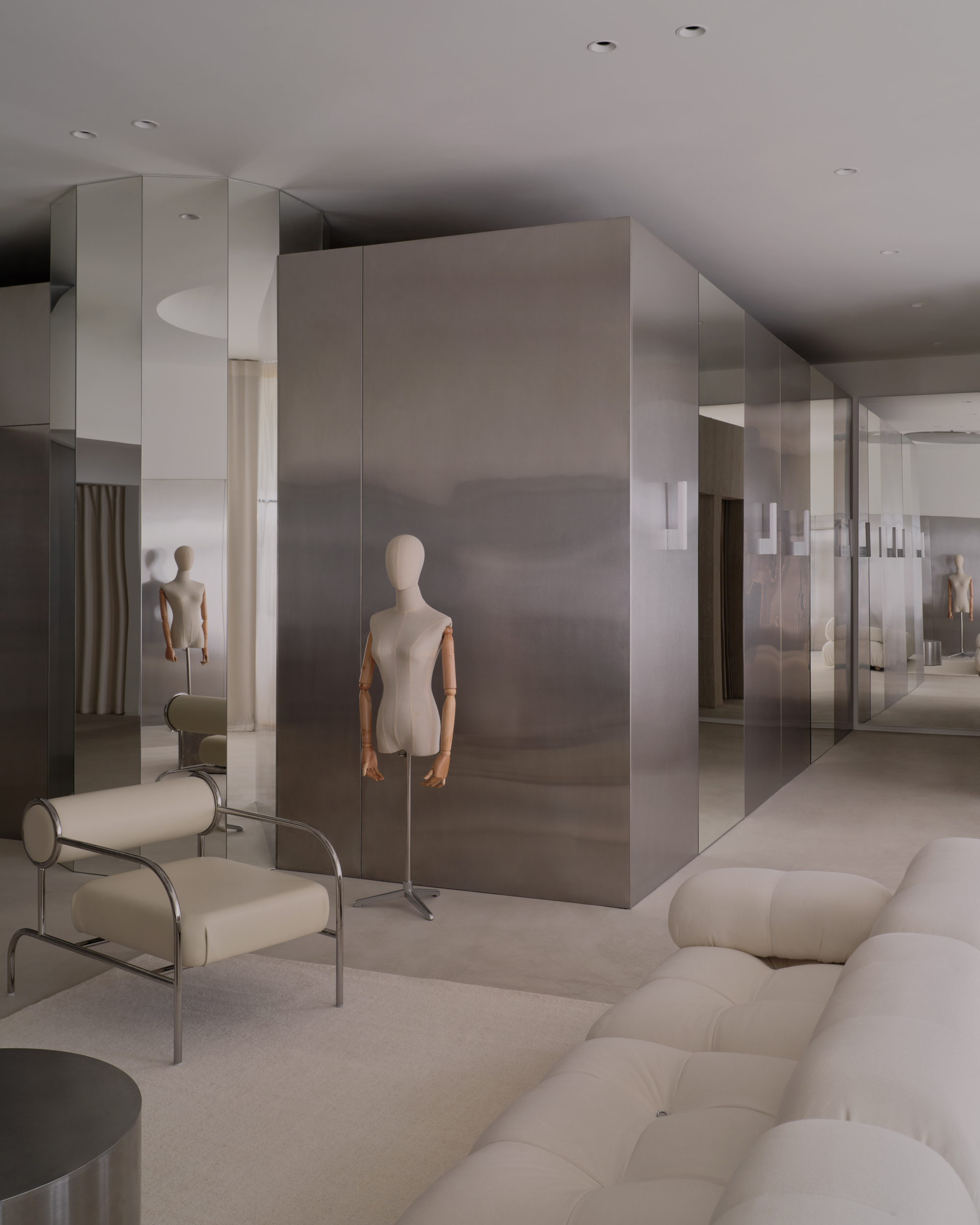 Mirrored partition wall reflecting mannequins and tubular steel chairs across the carpeted showroom floor