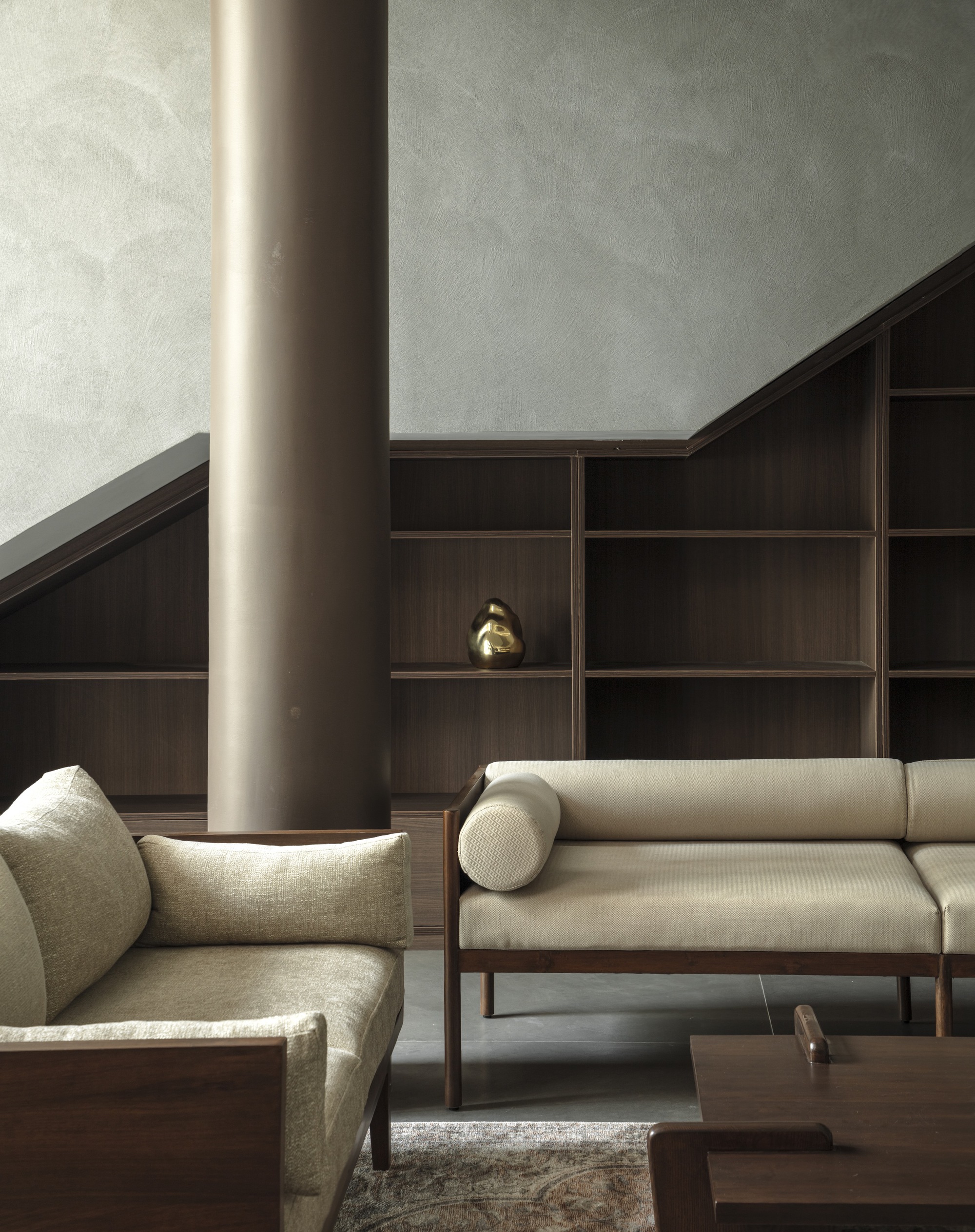 Close-up of cylindrical column beside timber-framed sofa and gridded shelving with small brass object