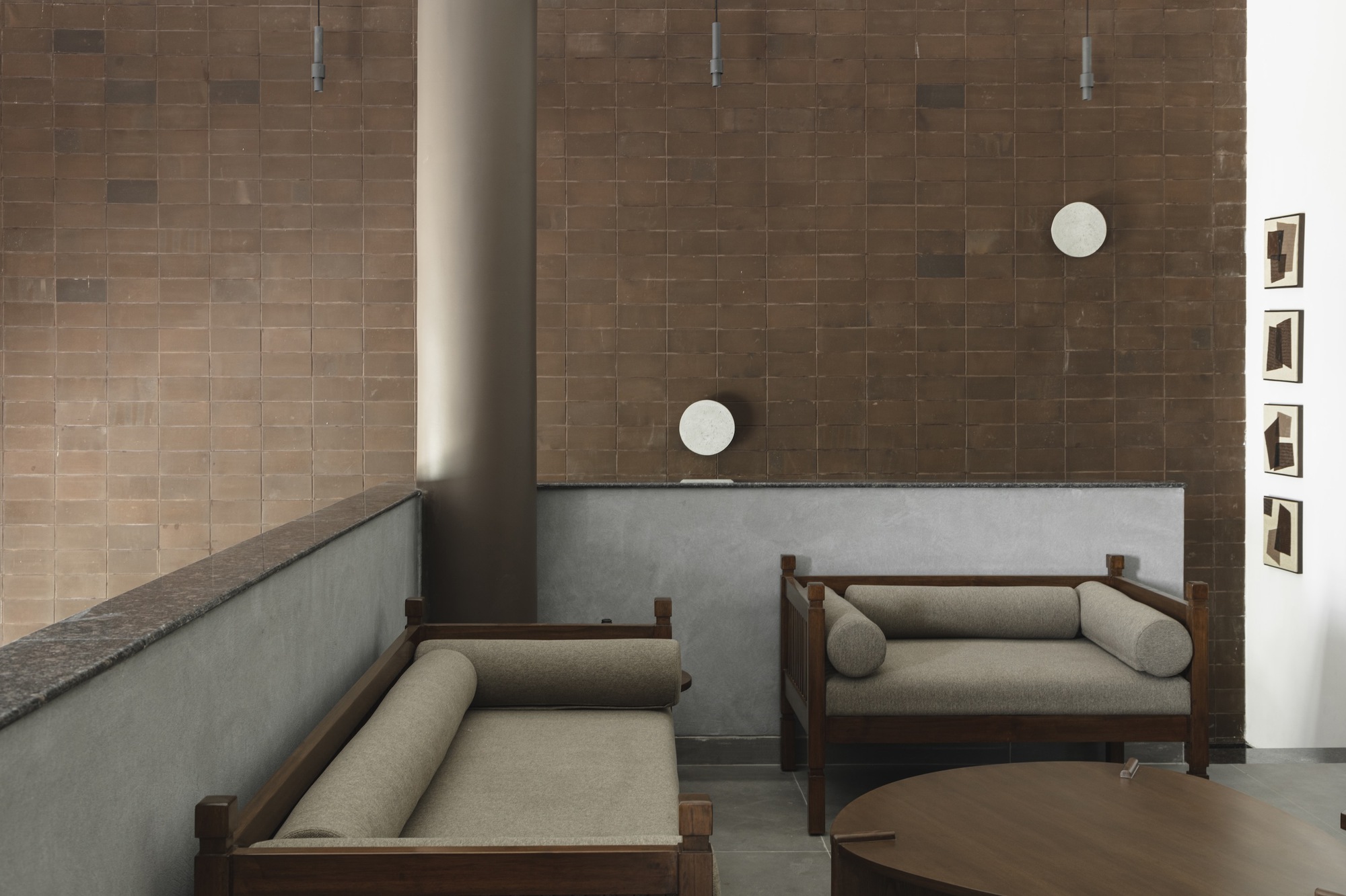 Seating area with brown tile wall and cylindrical column rising through polished concrete floor
