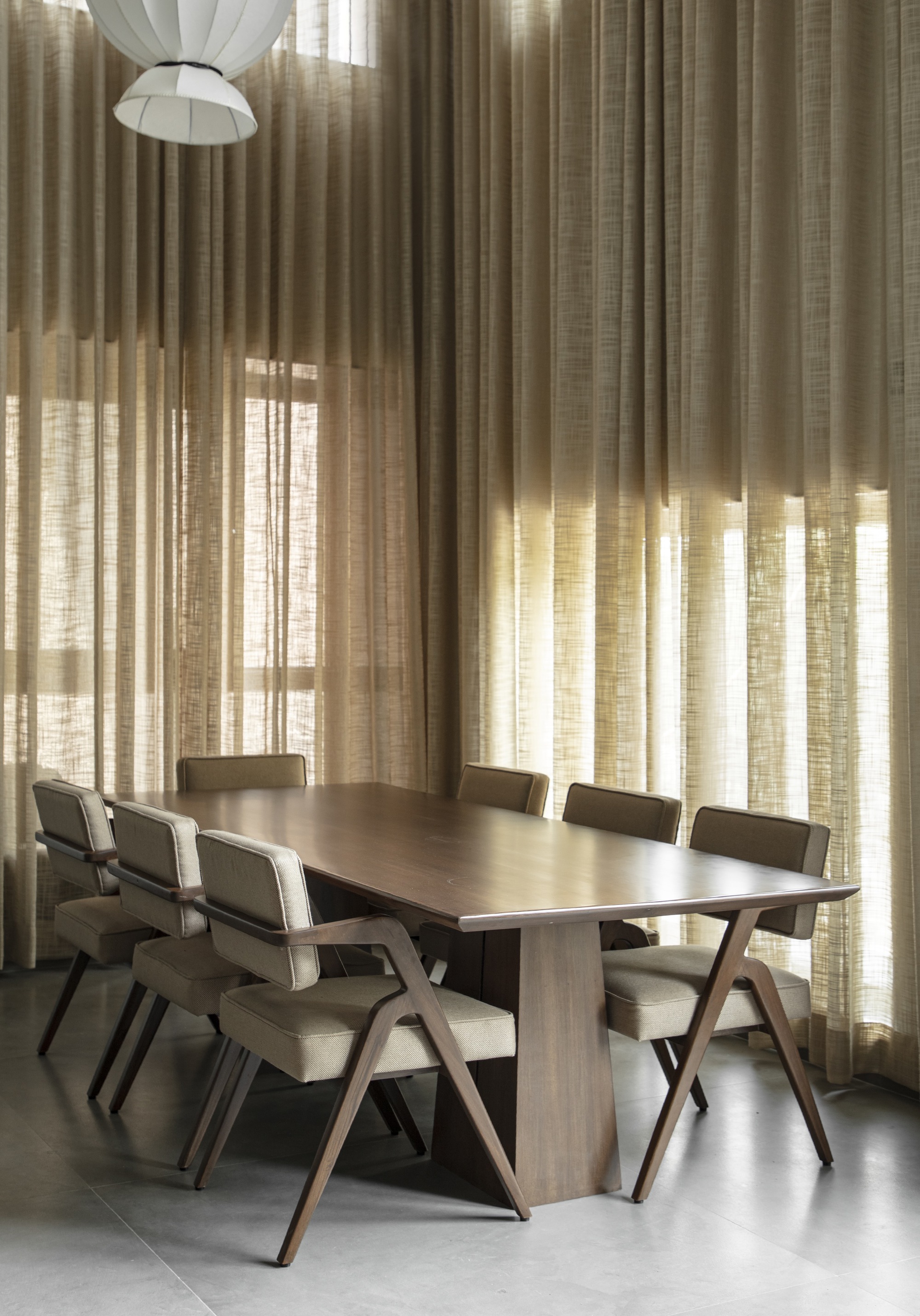 Dining area with timber table and chairs beneath layered linen curtains filtering soft daylight