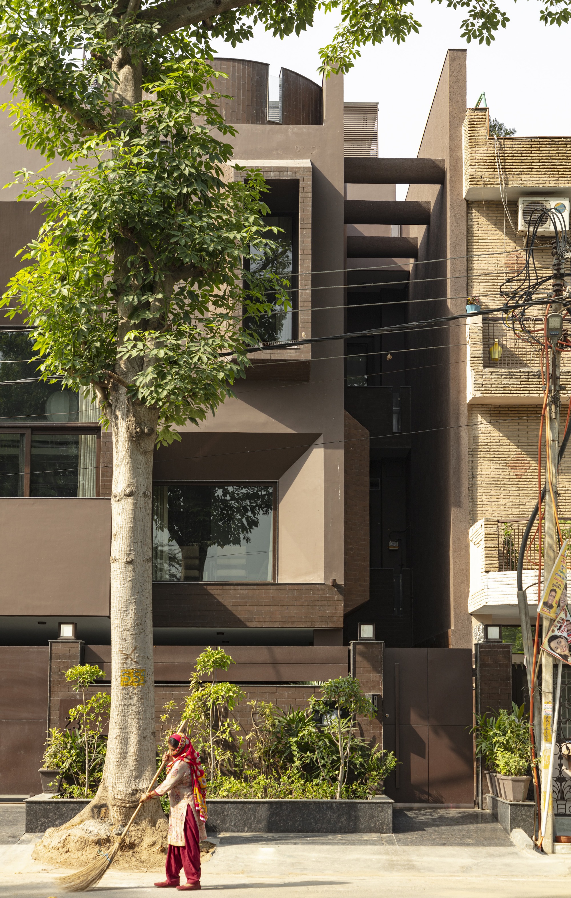 Street facade with layered volumes in plaster and brick framed by trees and a passing pedestrian