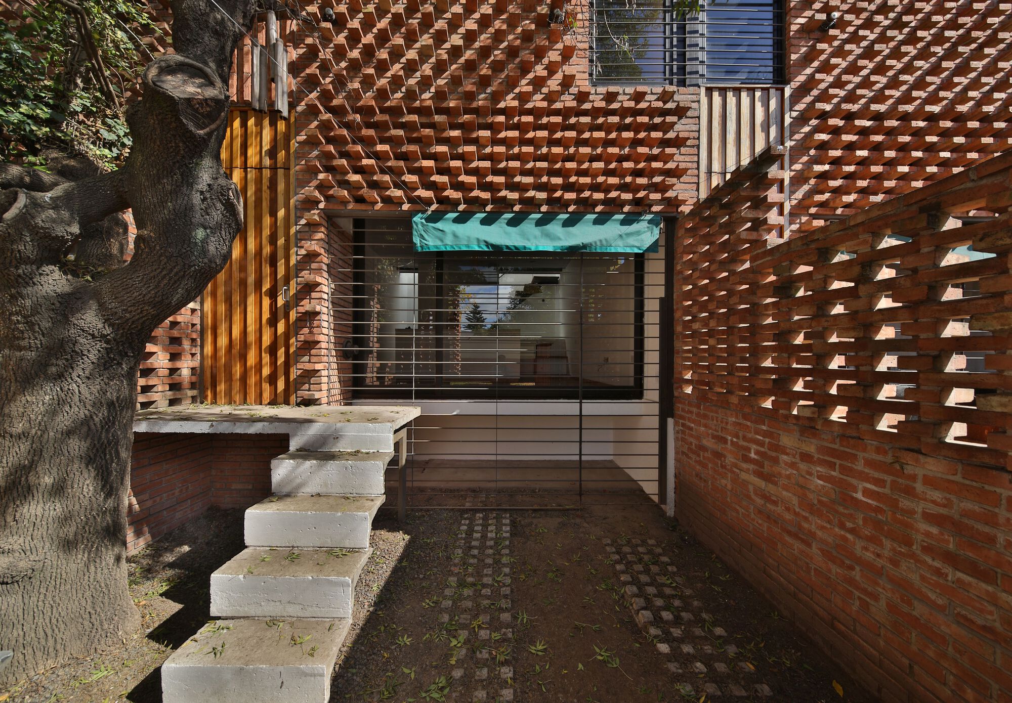 Courtyard entry with patterned brick walls and concrete steps flanked by an old tree