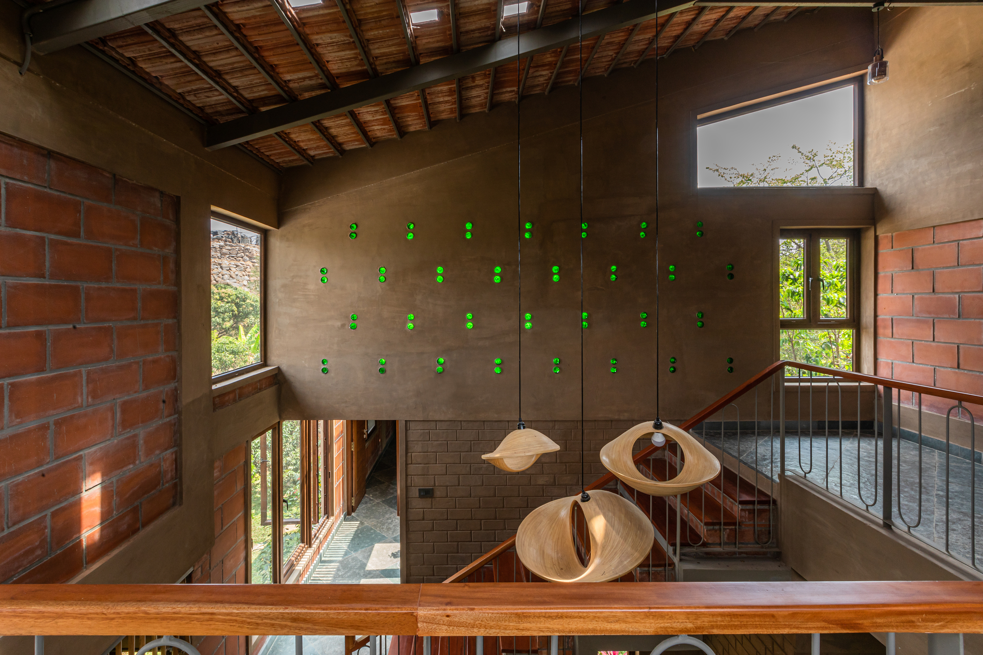 Double-height interior with timber ceiling beams, clay brick walls, pendant lights, and metal railings around a central void
