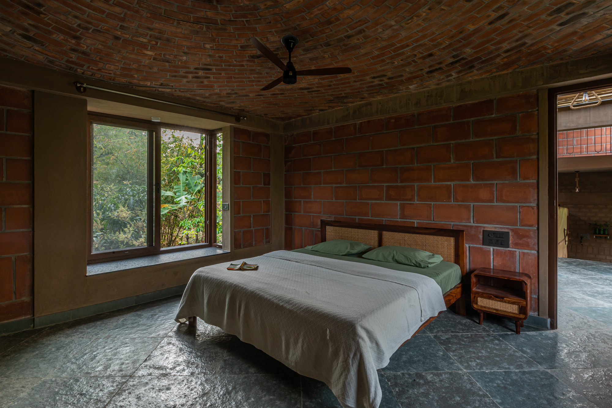 Bedroom with exposed red brick walls and vaulted ceiling with a window overlooking green foliage