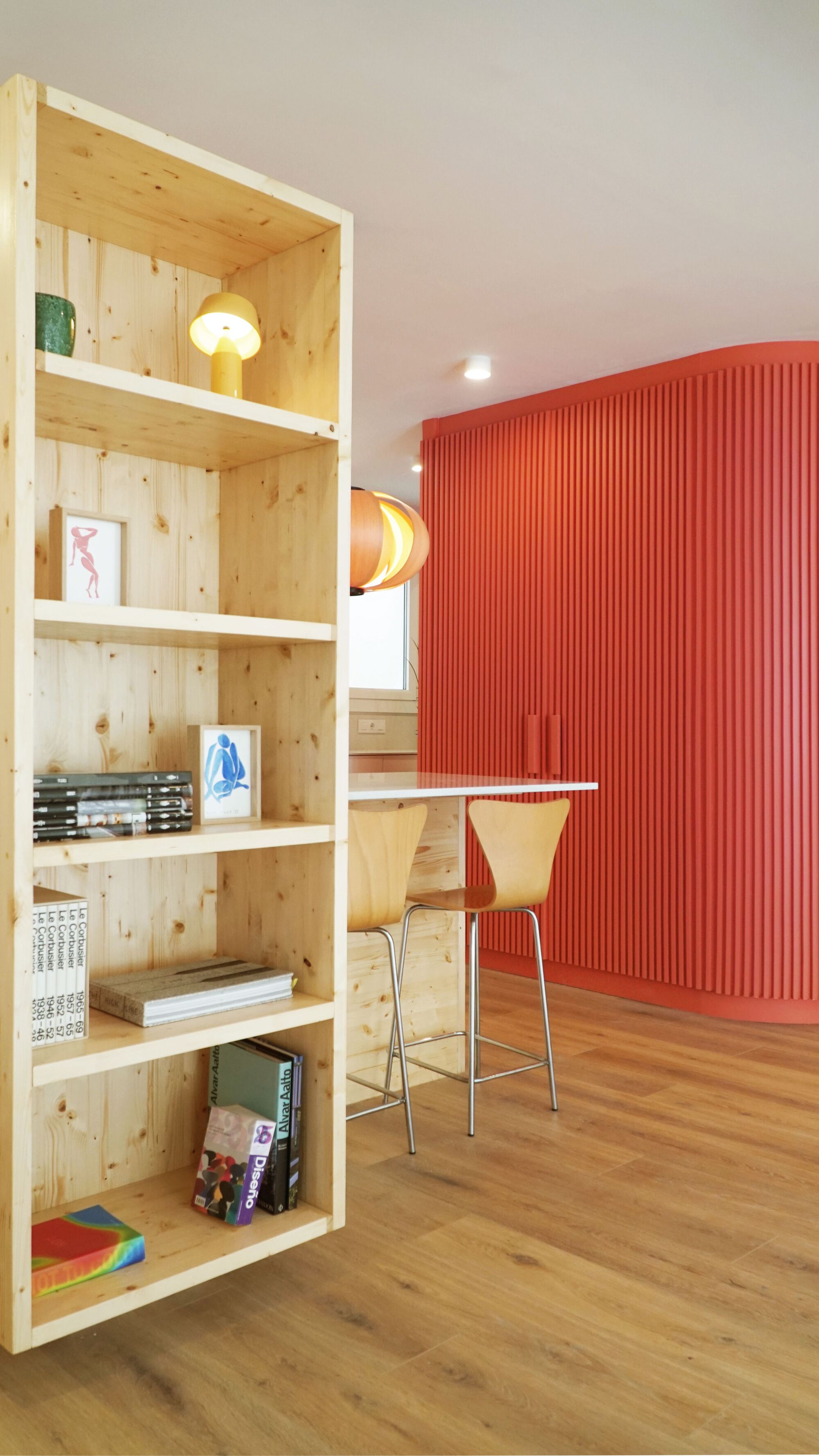 Pine plywood bookshelf beside a red fluted wall panel and a plywood-topped kitchen counter