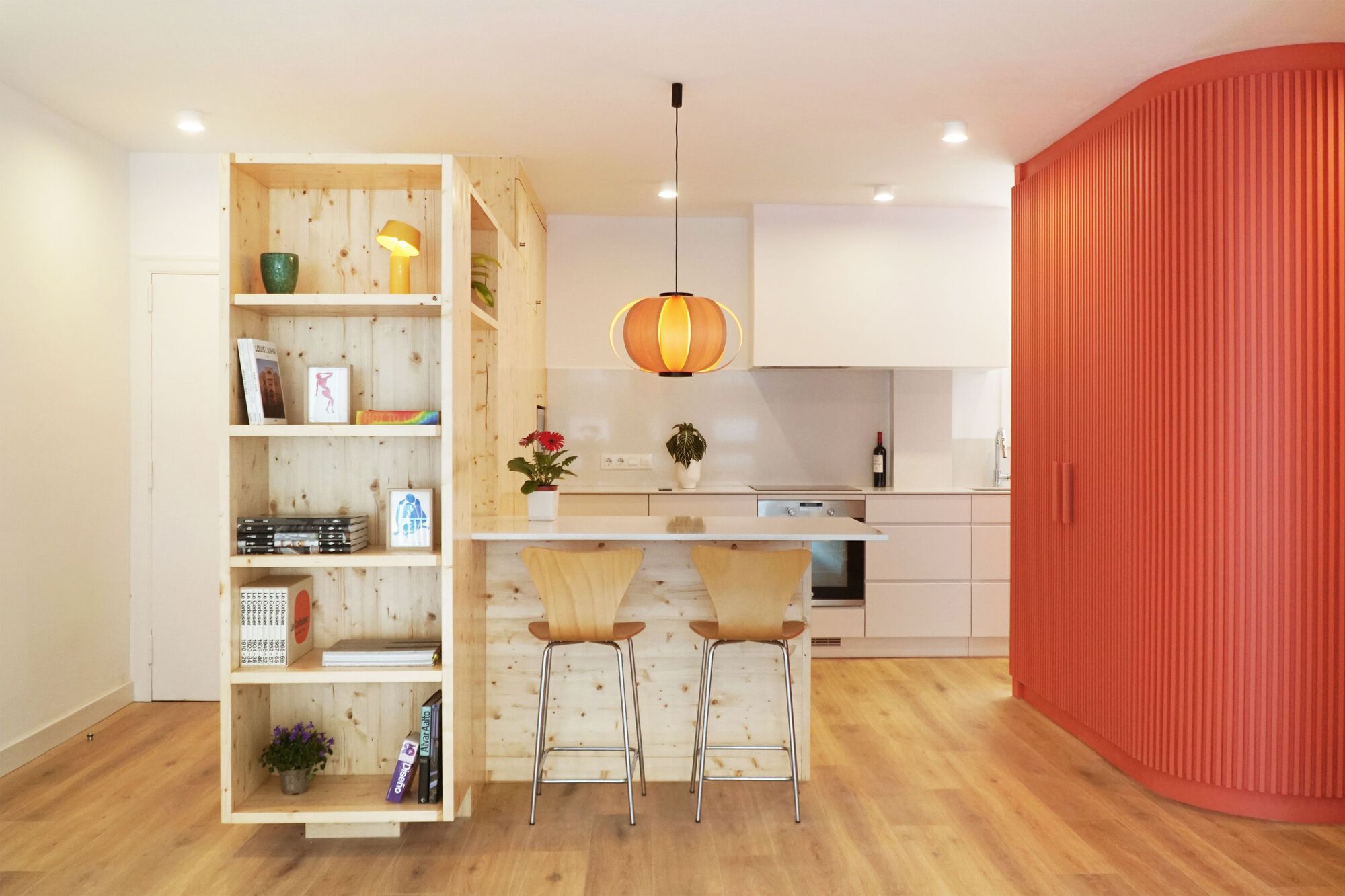 Open-plan kitchen with pine shelving unit and fluted orange cabinet wall in recessed lighting
