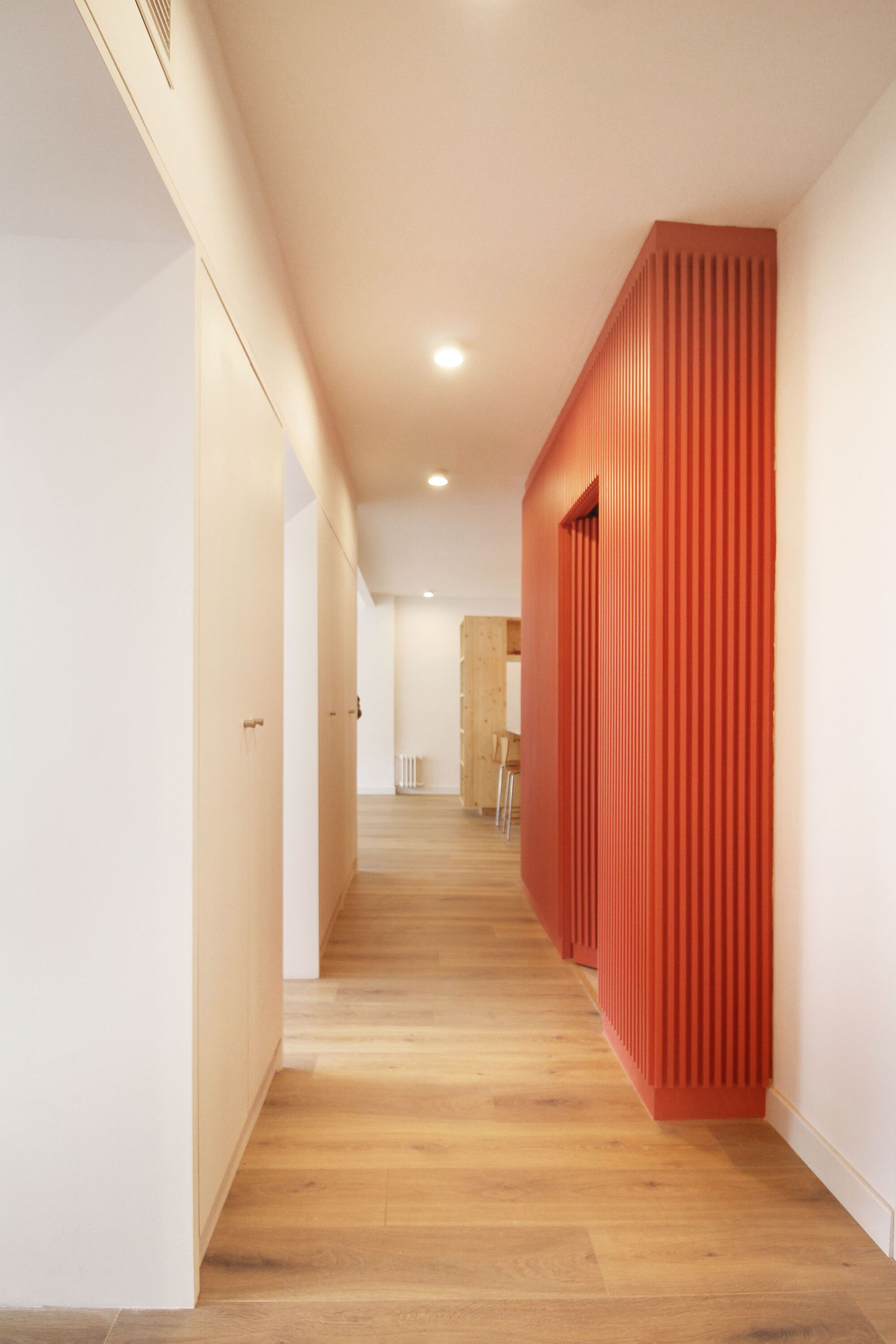 Hallway view along white walls with curved fluted orange volume and light oak flooring
