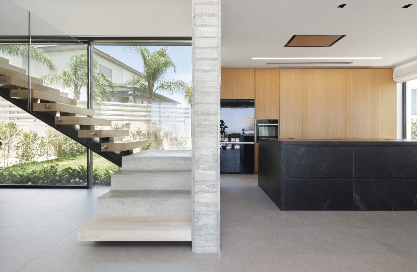 Open kitchen with black marble island adjacent to floating concrete stair and glass balustrade