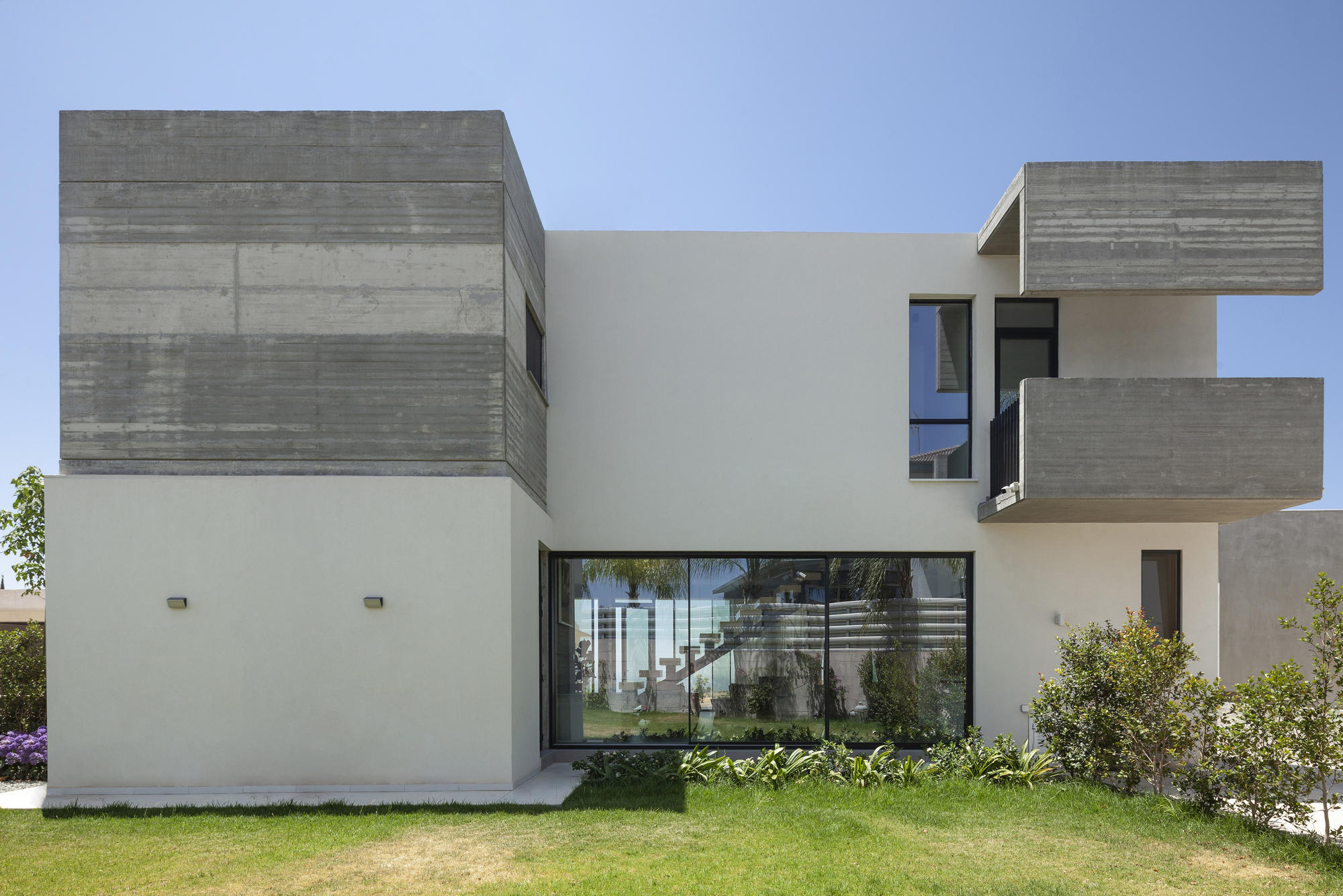 Garden facade showing interlocking white stucco and board-formed concrete volumes under blue sky