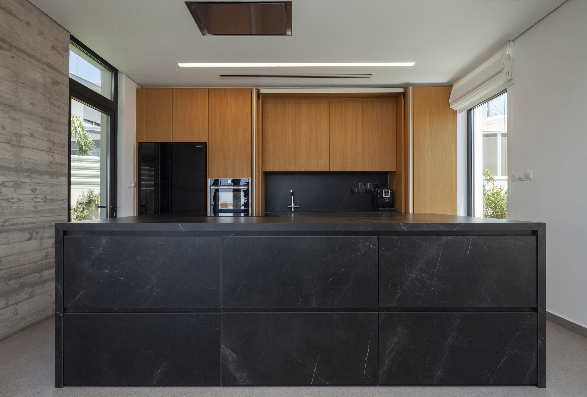 Open wood cabinetry revealing dark backsplash and sink with marble-clad island in foreground