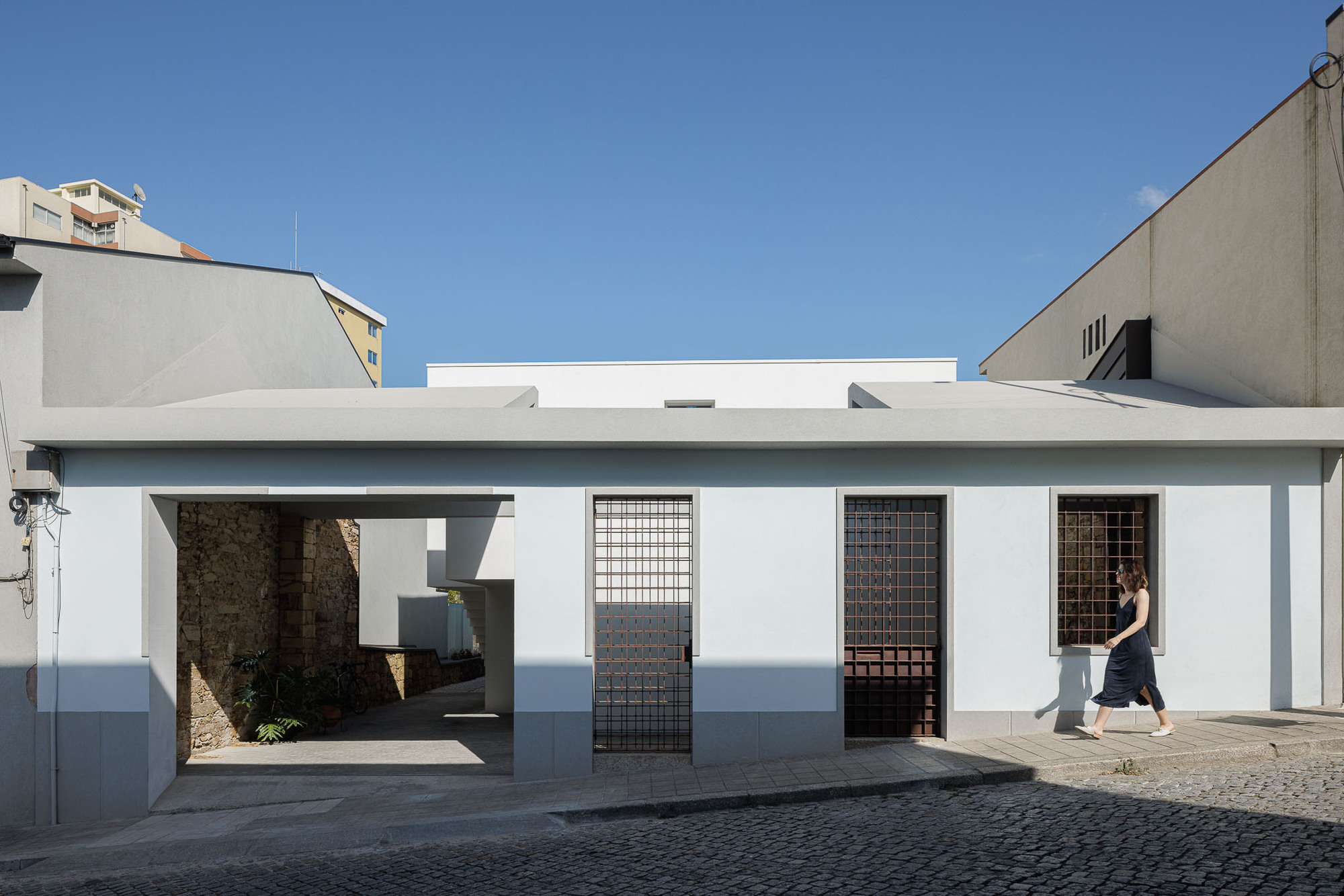 Street facade with white stucco and gridded metal screen doors beneath a clear blue sky