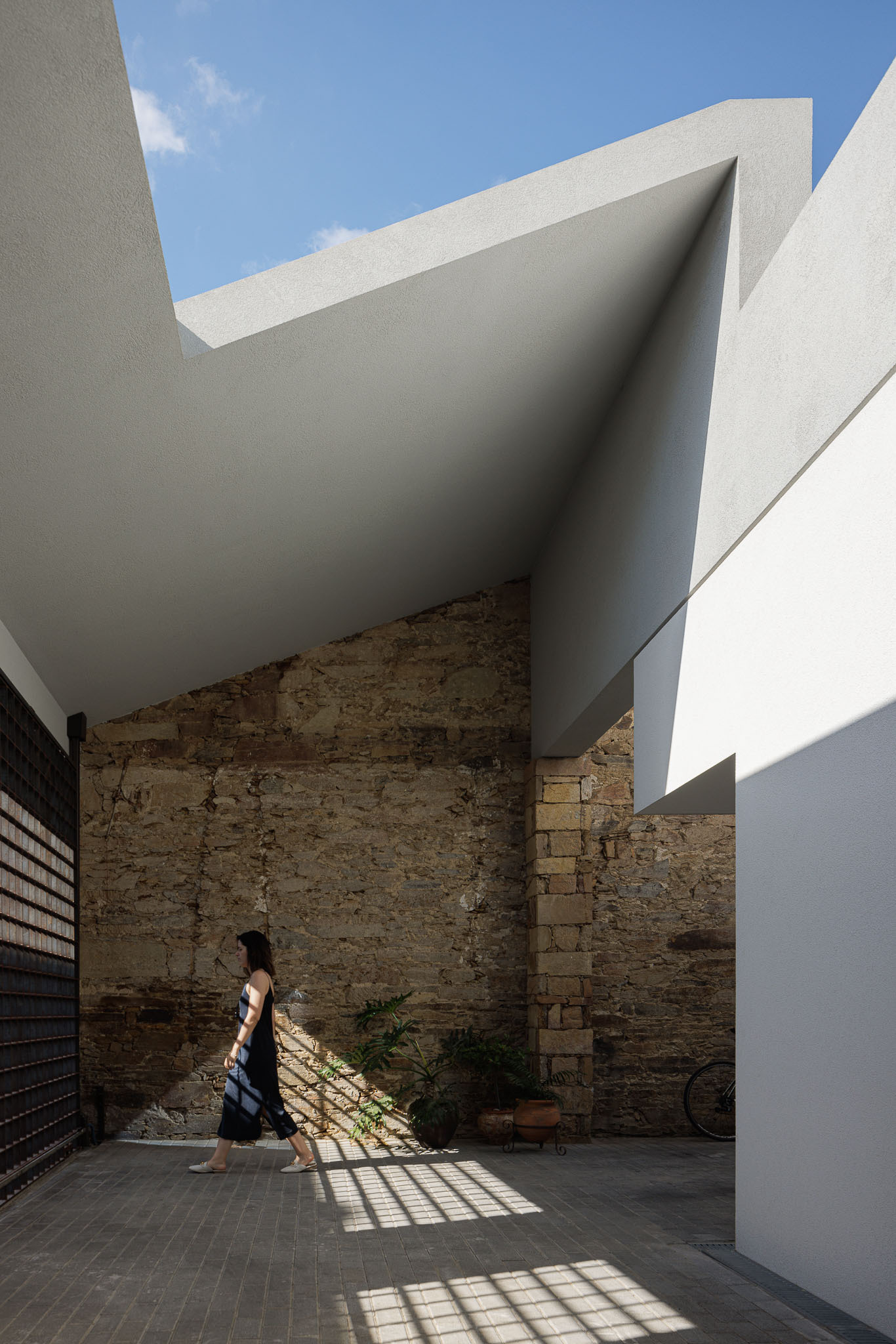 Figure walking through courtyard where gridded screen casts geometric shadows on brick paving