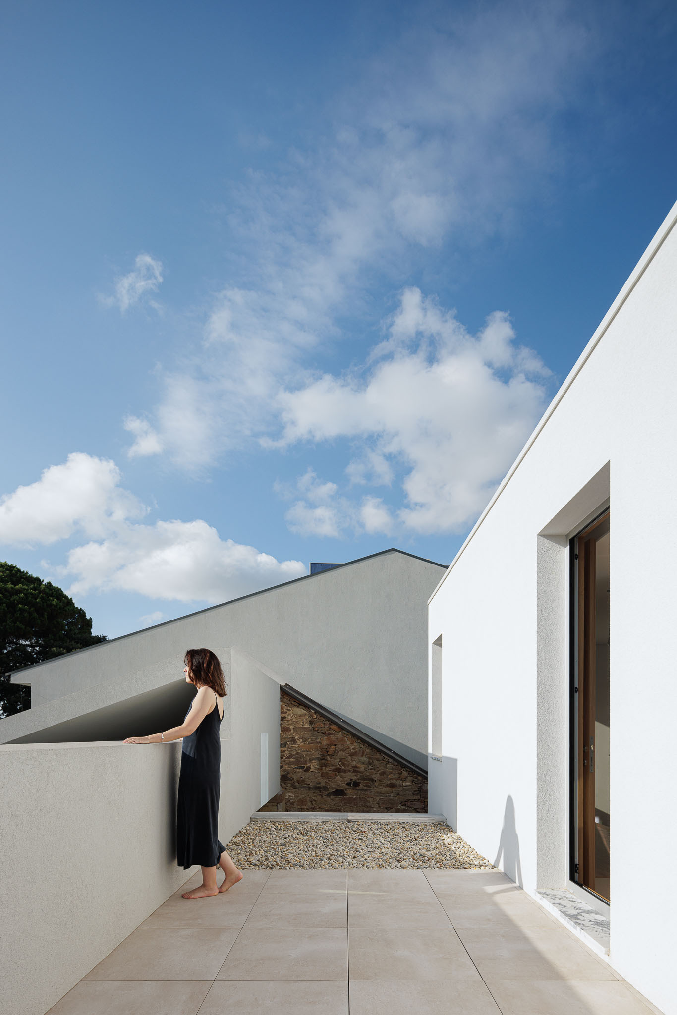 Rooftop terrace with gravel surface and woman in black dress under scattered afternoon clouds