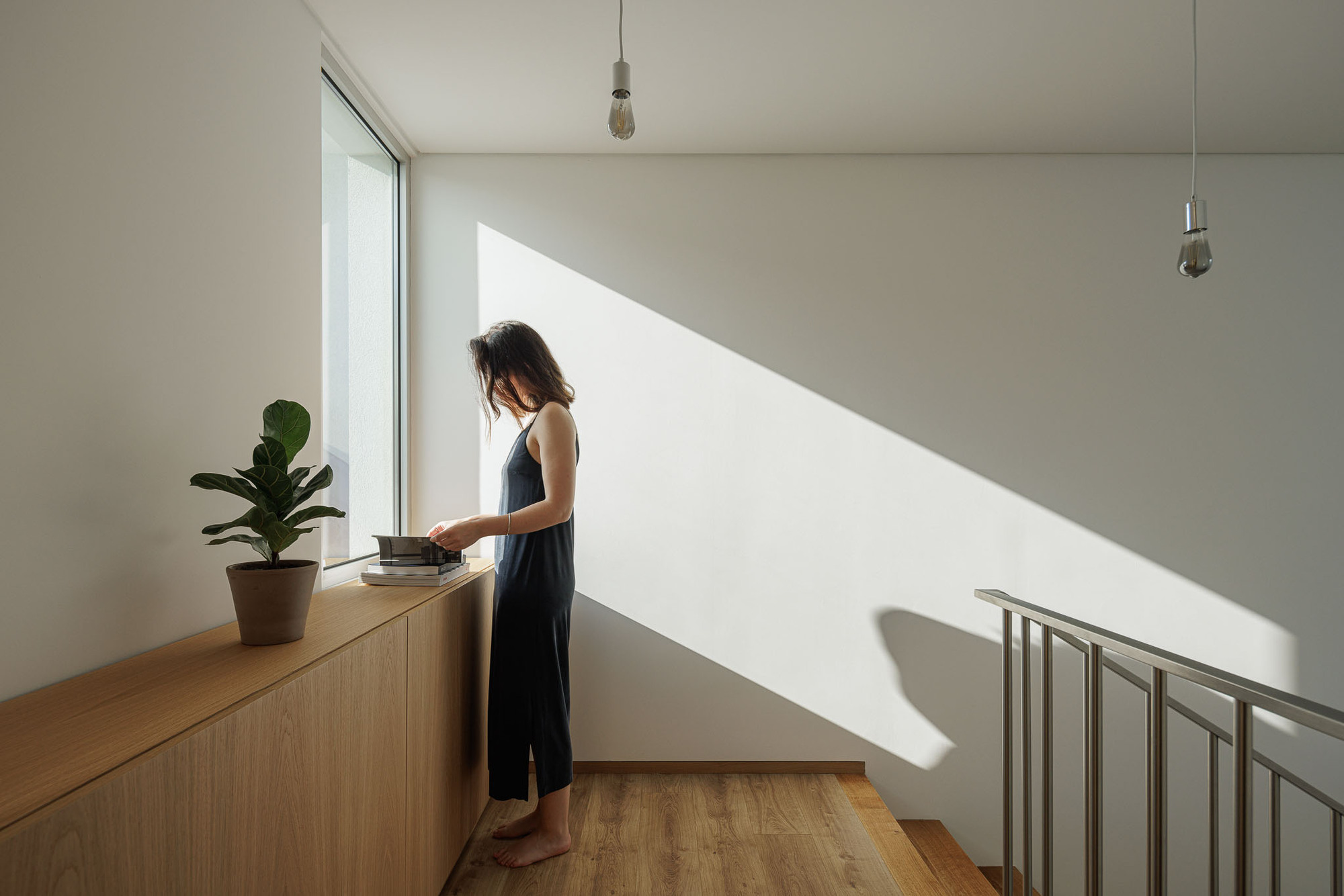 Upper landing with low timber counter beside window casting sharp diagonal sunlight across white wall