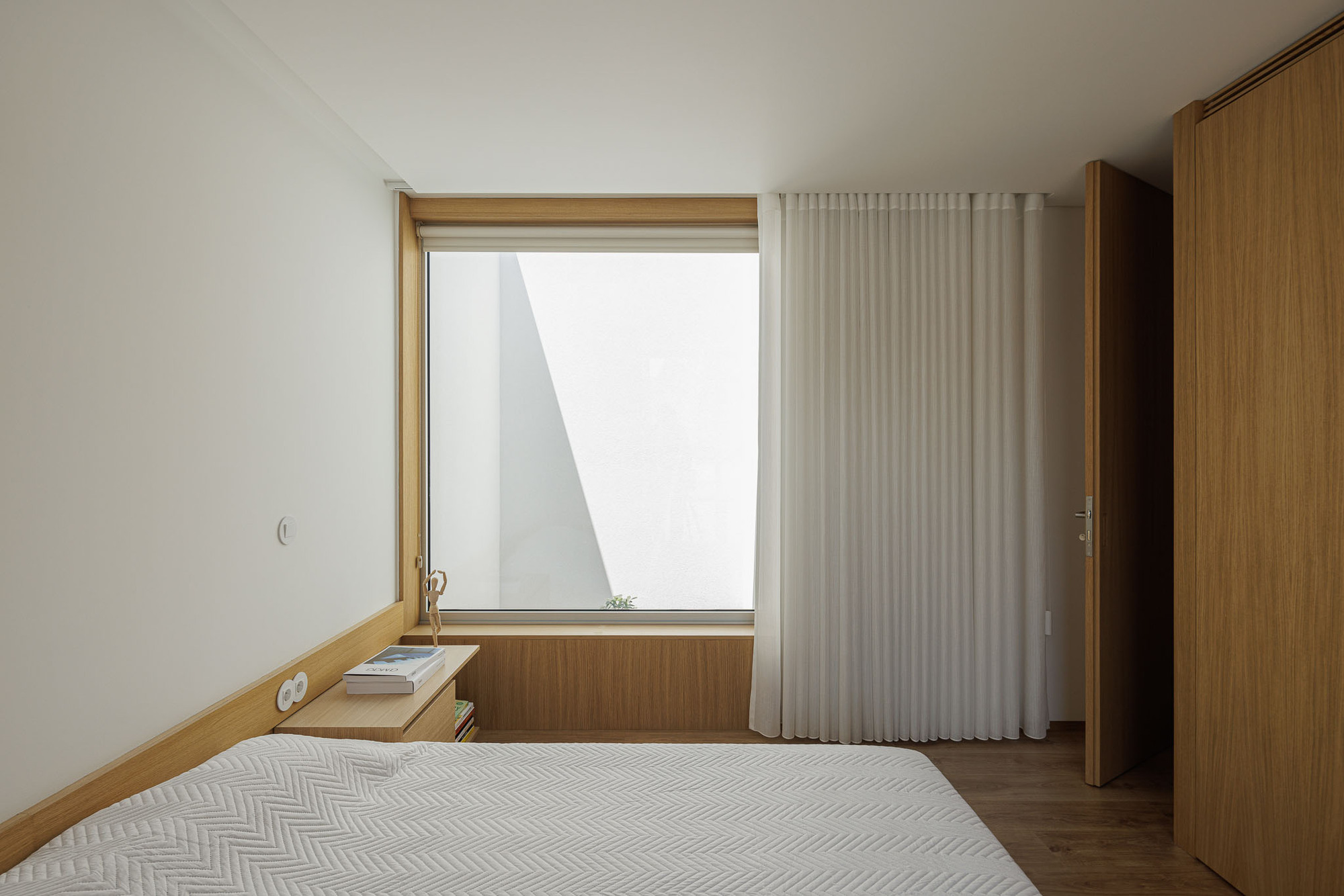Bedroom with timber-framed window and white curtain partially drawn beneath sloped ceiling
