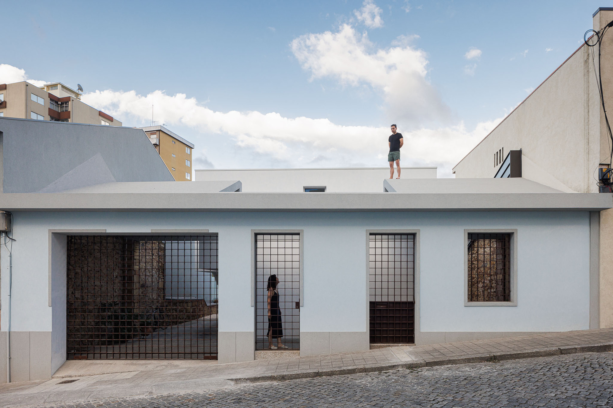 Street facade with white stucco walls and metal grille doors with a figure on the rooftop