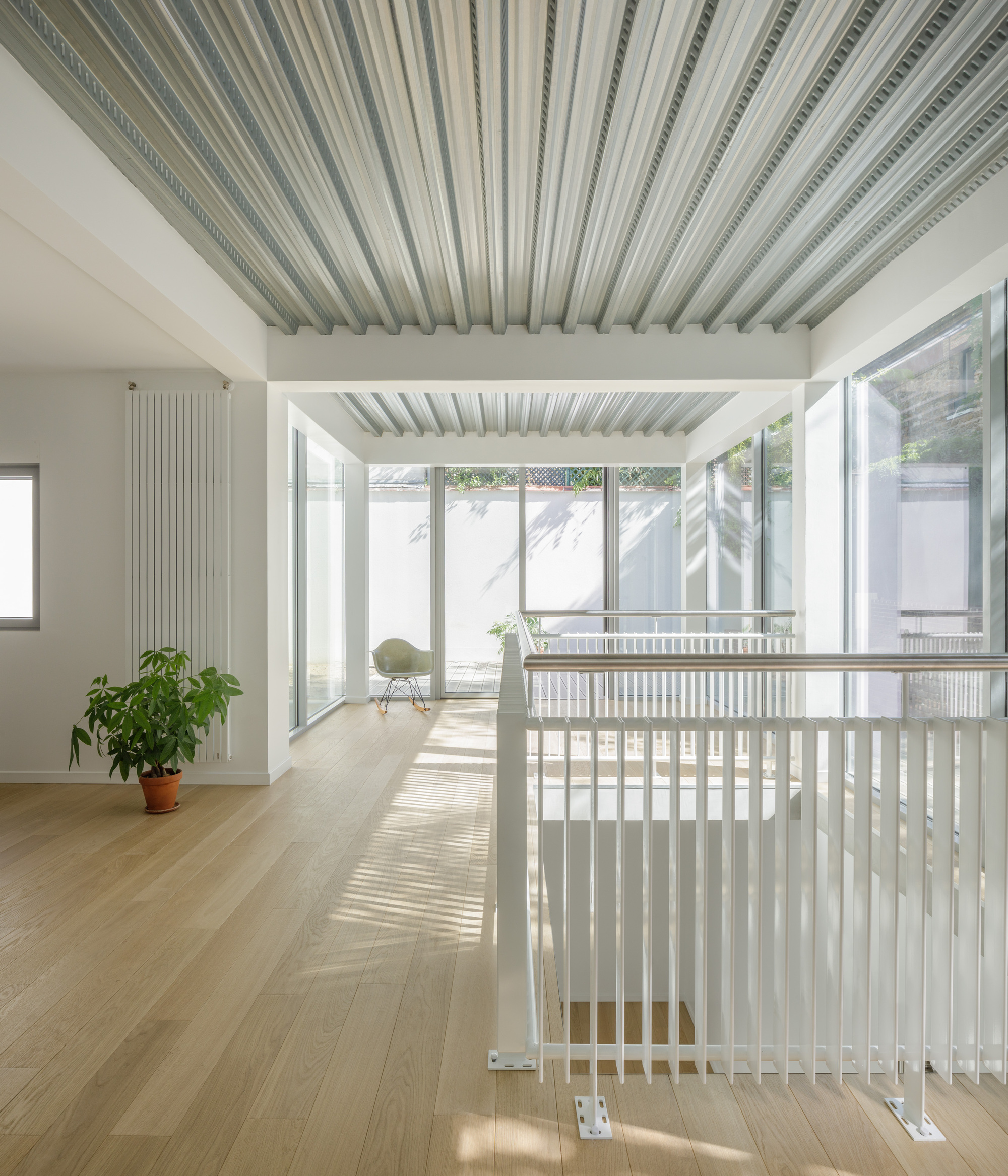 White painted timber balustrade bordering stairwell opening with striped ceiling panels above and courtyard beyond