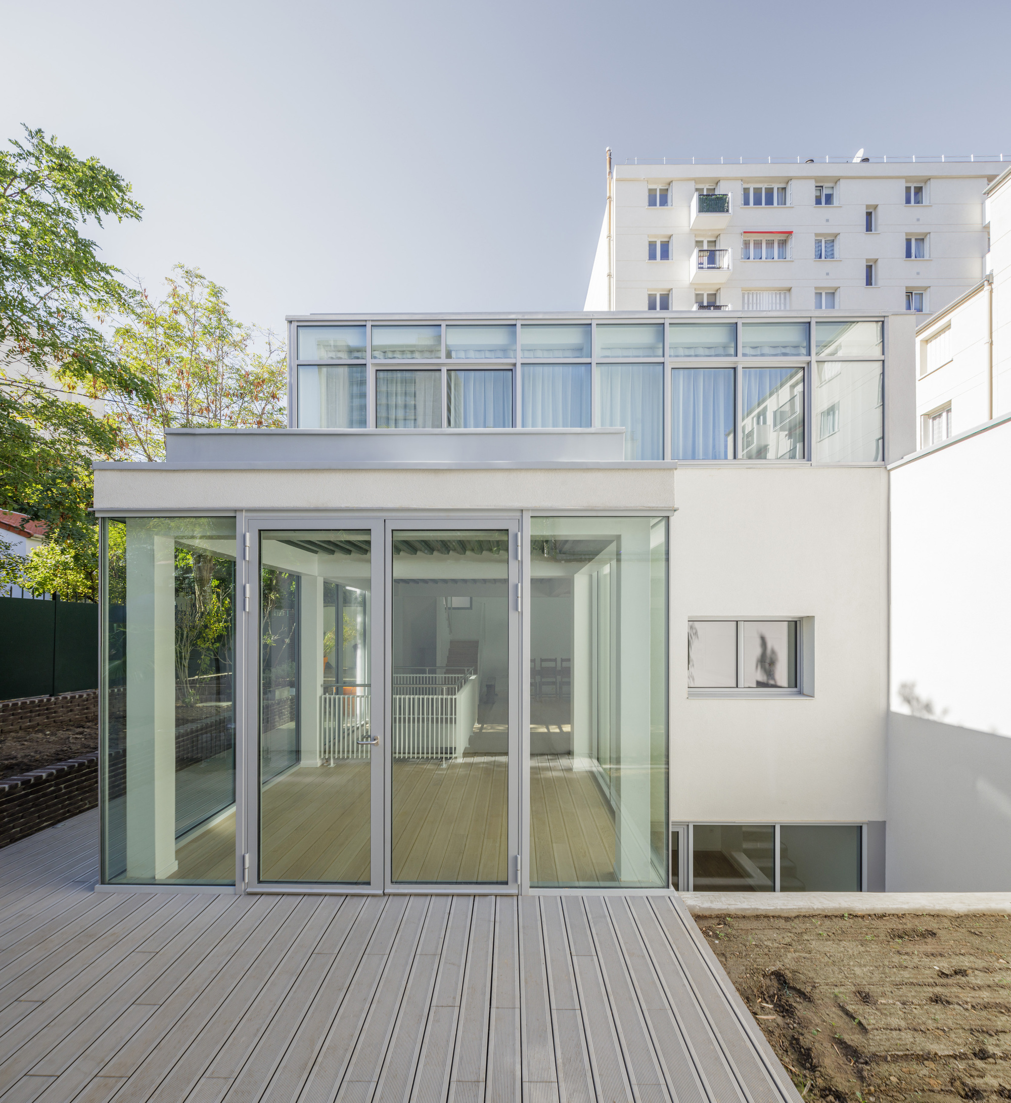 Rear facade with full-height glazing opening onto a timber deck beside a planted garden bed