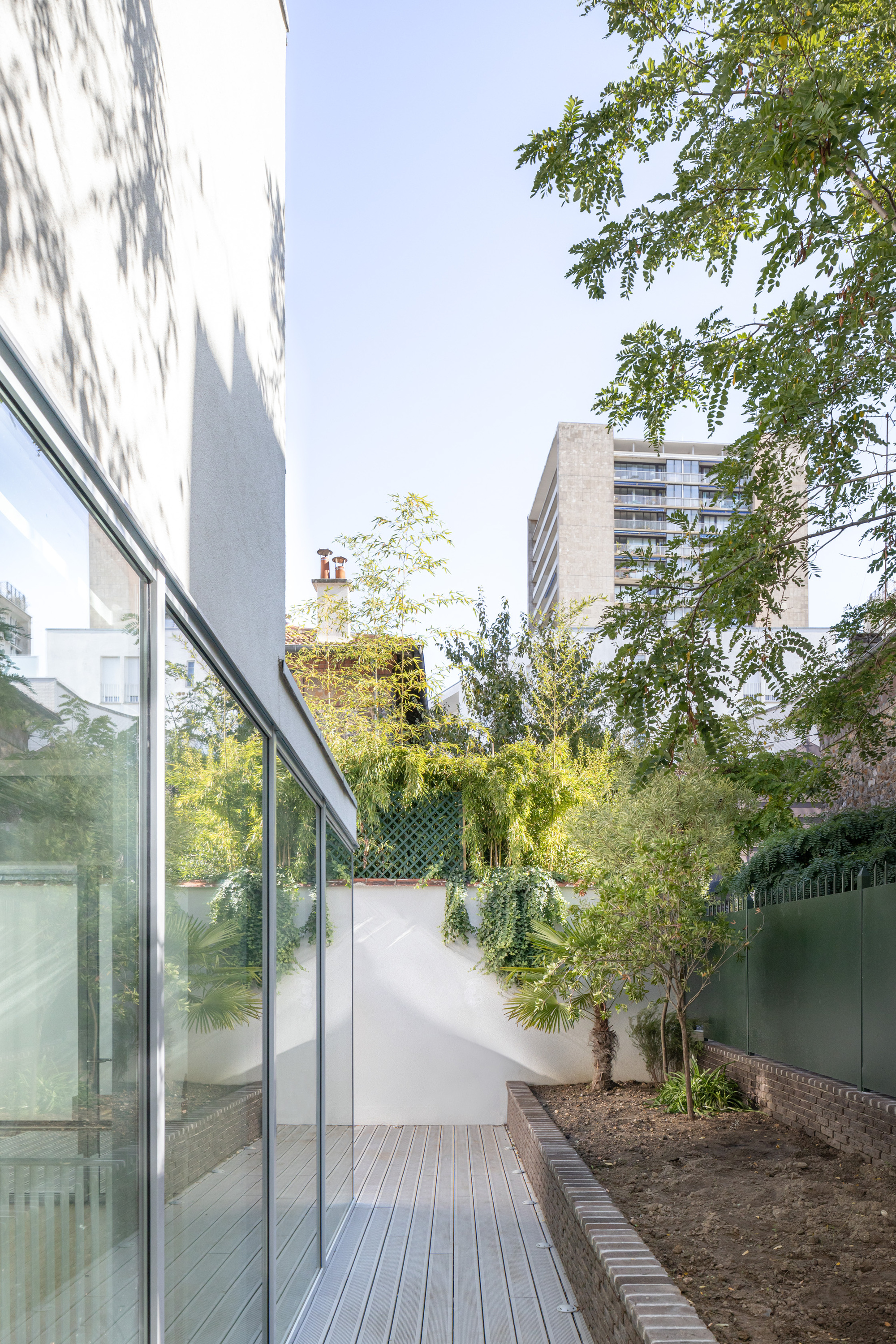 Glazed extension along a timber deck looking toward an ivy-covered garden wall and trees beyond