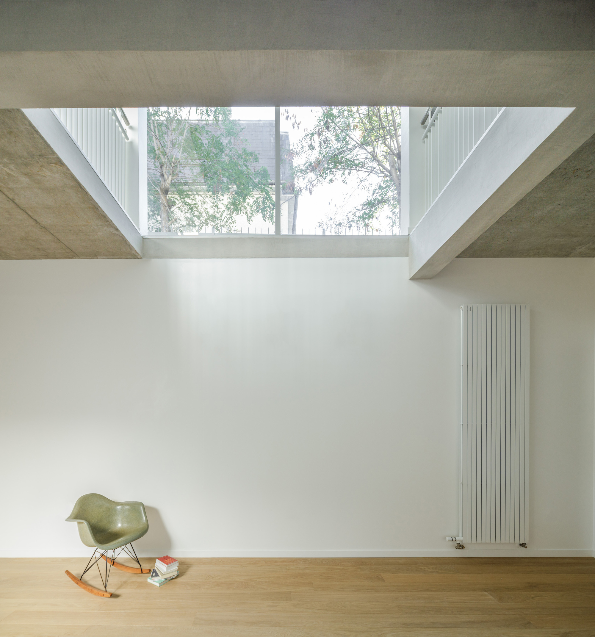 Interior room with clerestory window framing tree canopy above a vertical radiator and timber floor