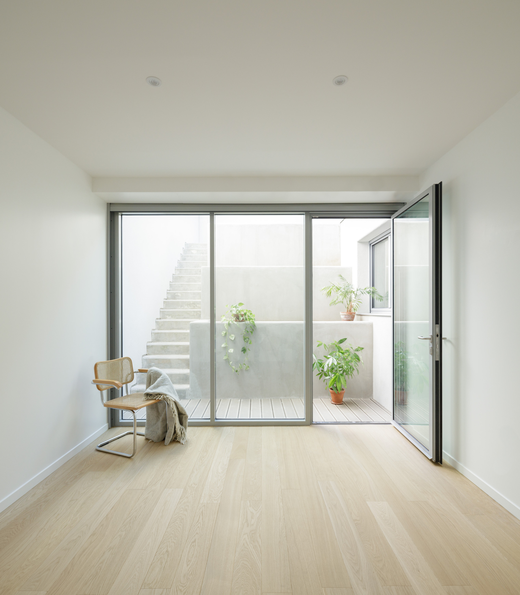 Room with glazed doors opening to a courtyard with timber decking, stair, and potted plants