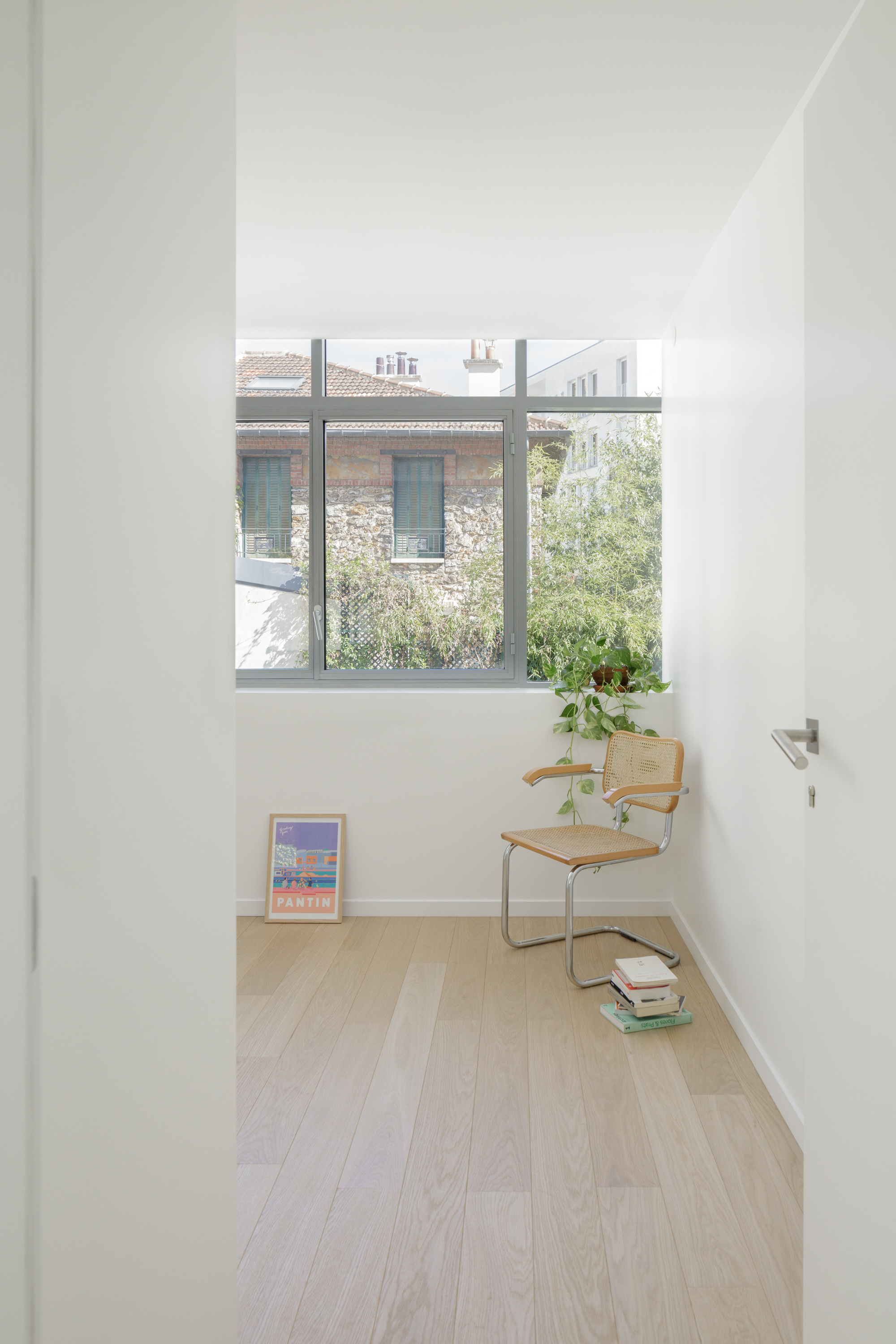 Narrow room with window overlooking a neighboring masonry building and garden in soft daylight
