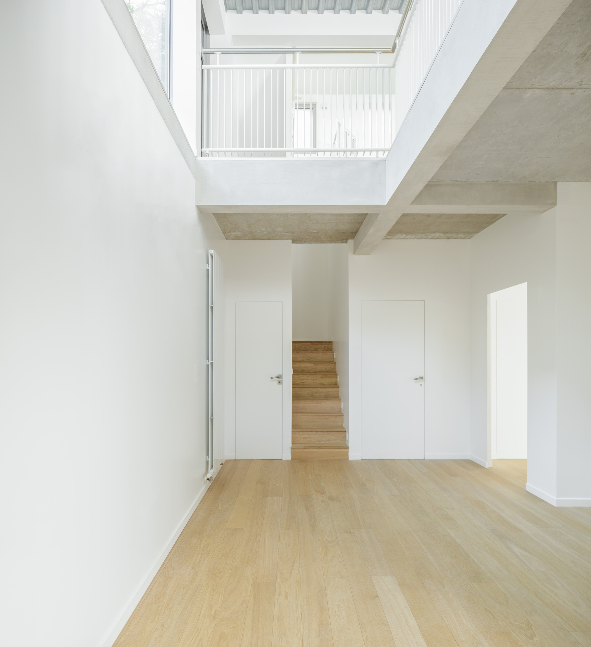Double-height living space with exposed concrete beams and skylight opening to upper floor balcony