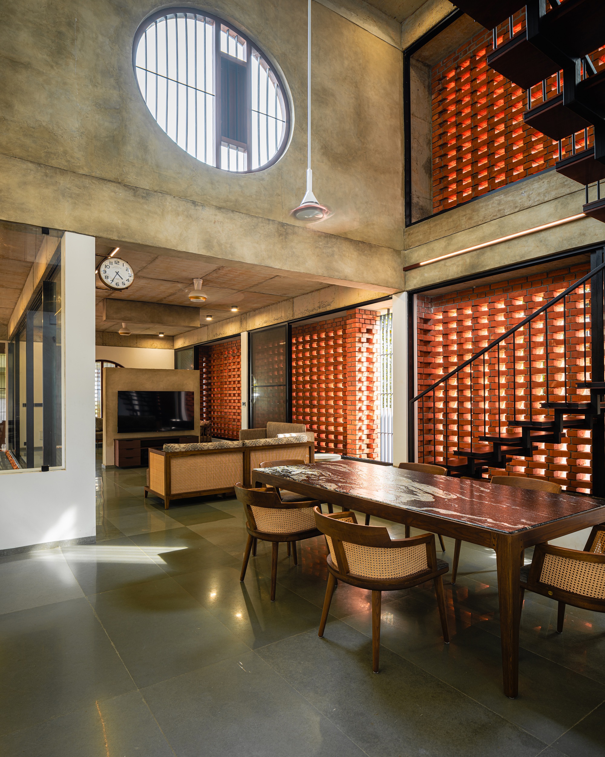 Double-height living and dining space with circular window above and perforated brick screens on two levels
