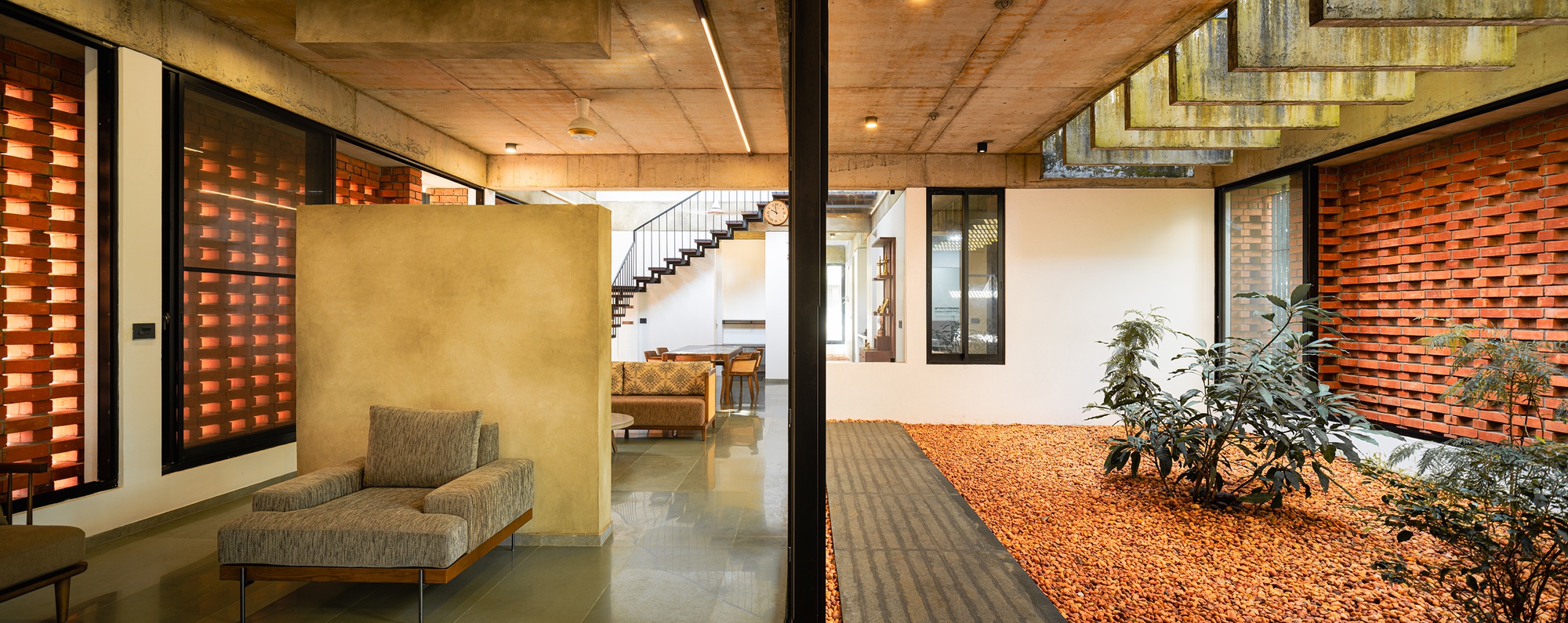 Living space opening onto gravel courtyard with staircase visible beyond concrete ceiling beams