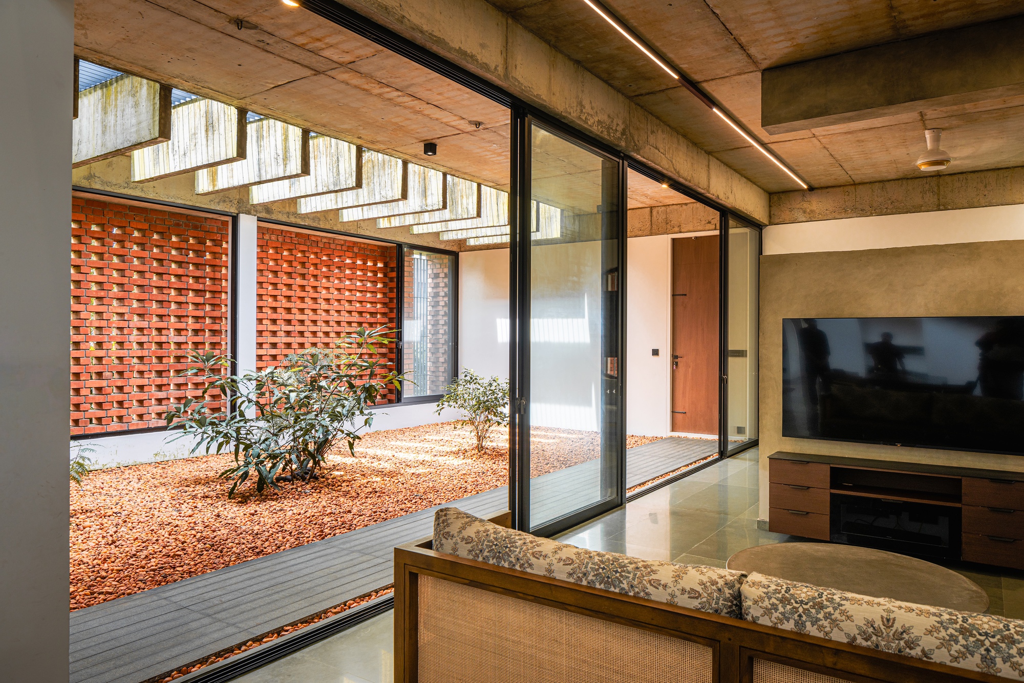 Living room overlooking the internal courtyard through floor-to-ceiling glazing with exposed concrete ceiling above