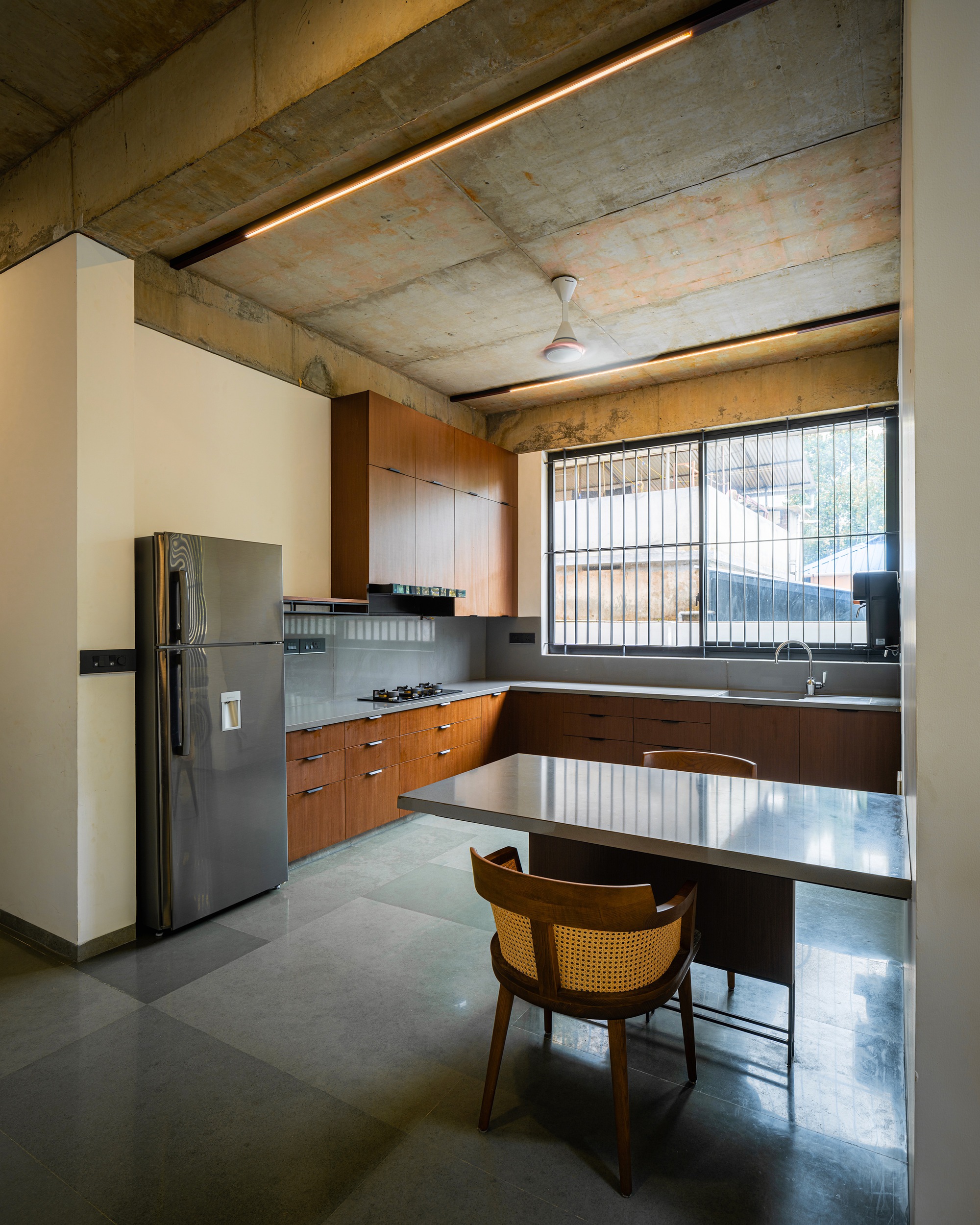 Kitchen with wood cabinetry and exposed concrete ceiling beams lit by recessed linear strips