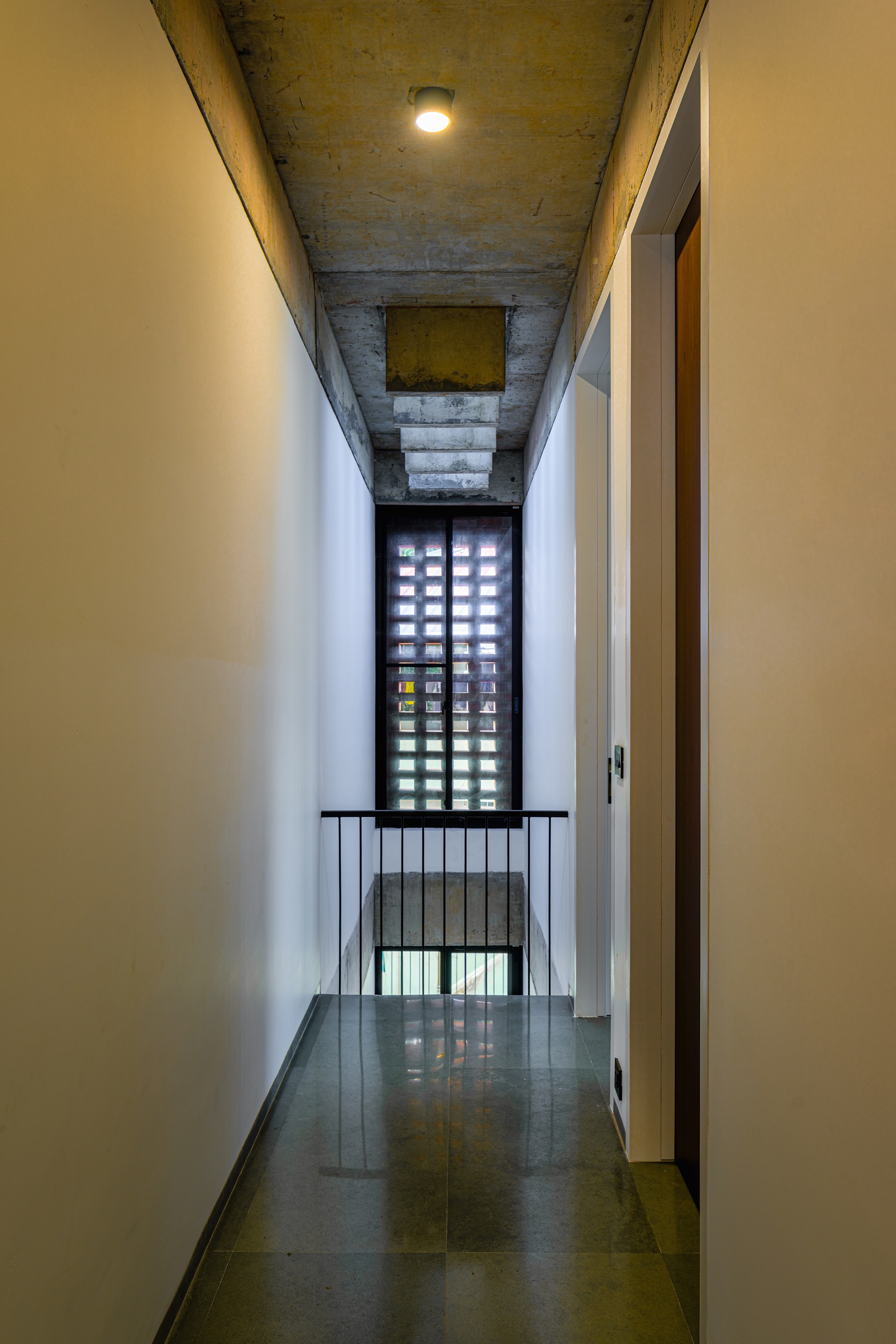 Narrow corridor with perforated screen wall at end and exposed concrete ceiling overhead