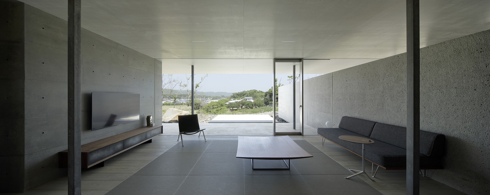 Living space with concrete walls and dark tile floor opening to landscape views through sliding glass