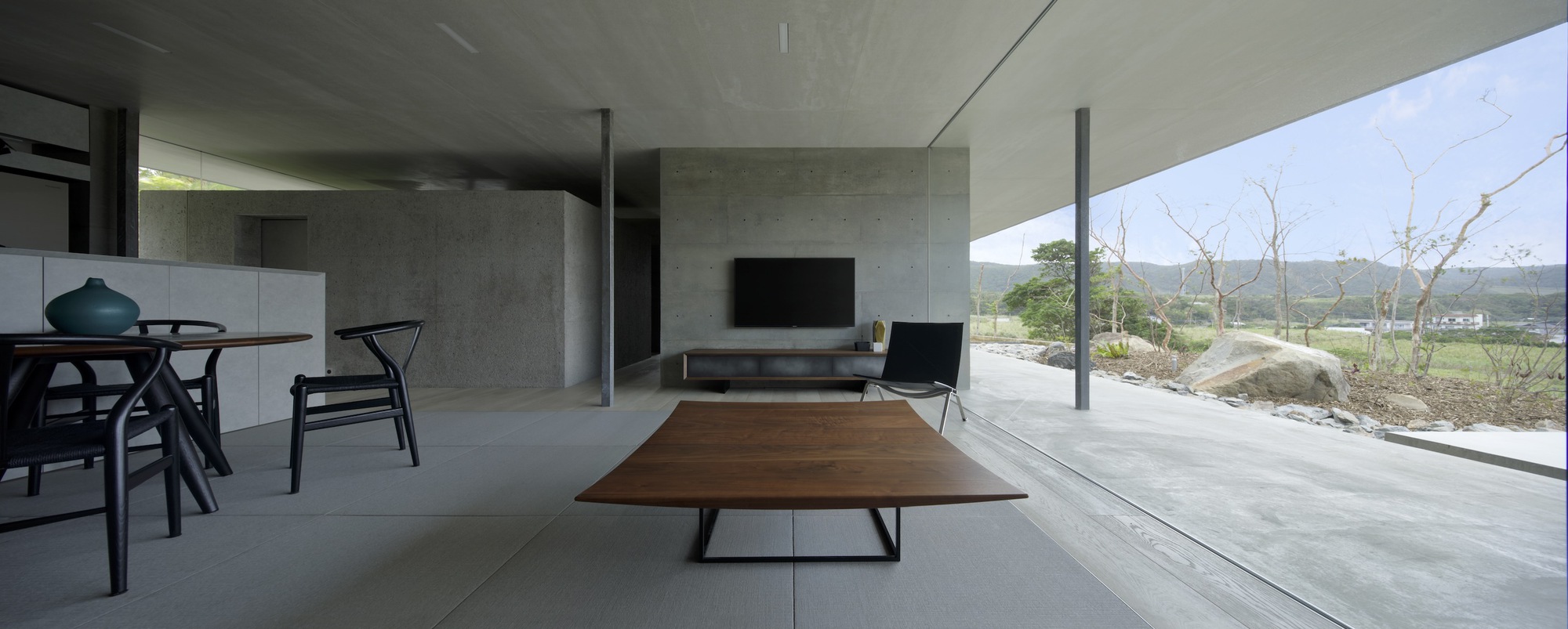 Interior view with walnut coffee table and glazed terrace overlooking low vegetation and distant hills