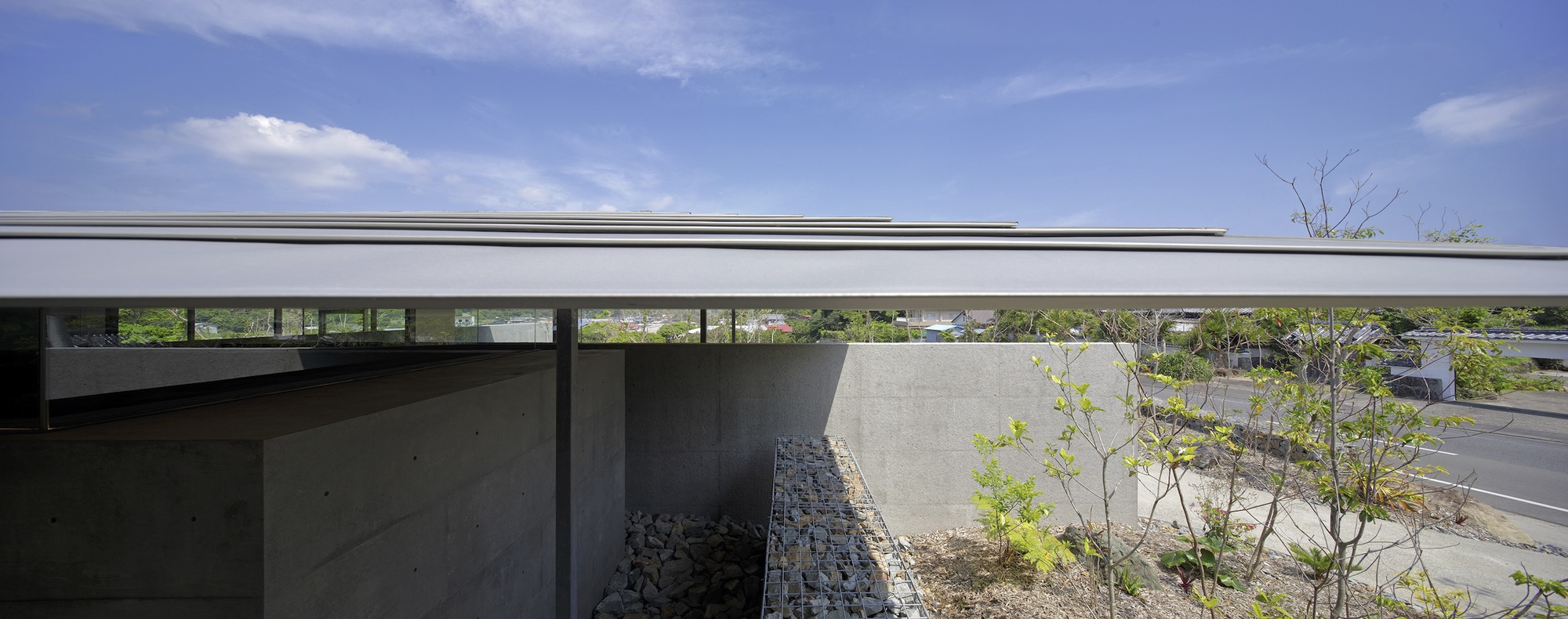 Low-profile flat roof extending over concrete walls and planted areas with young saplings in daylight
