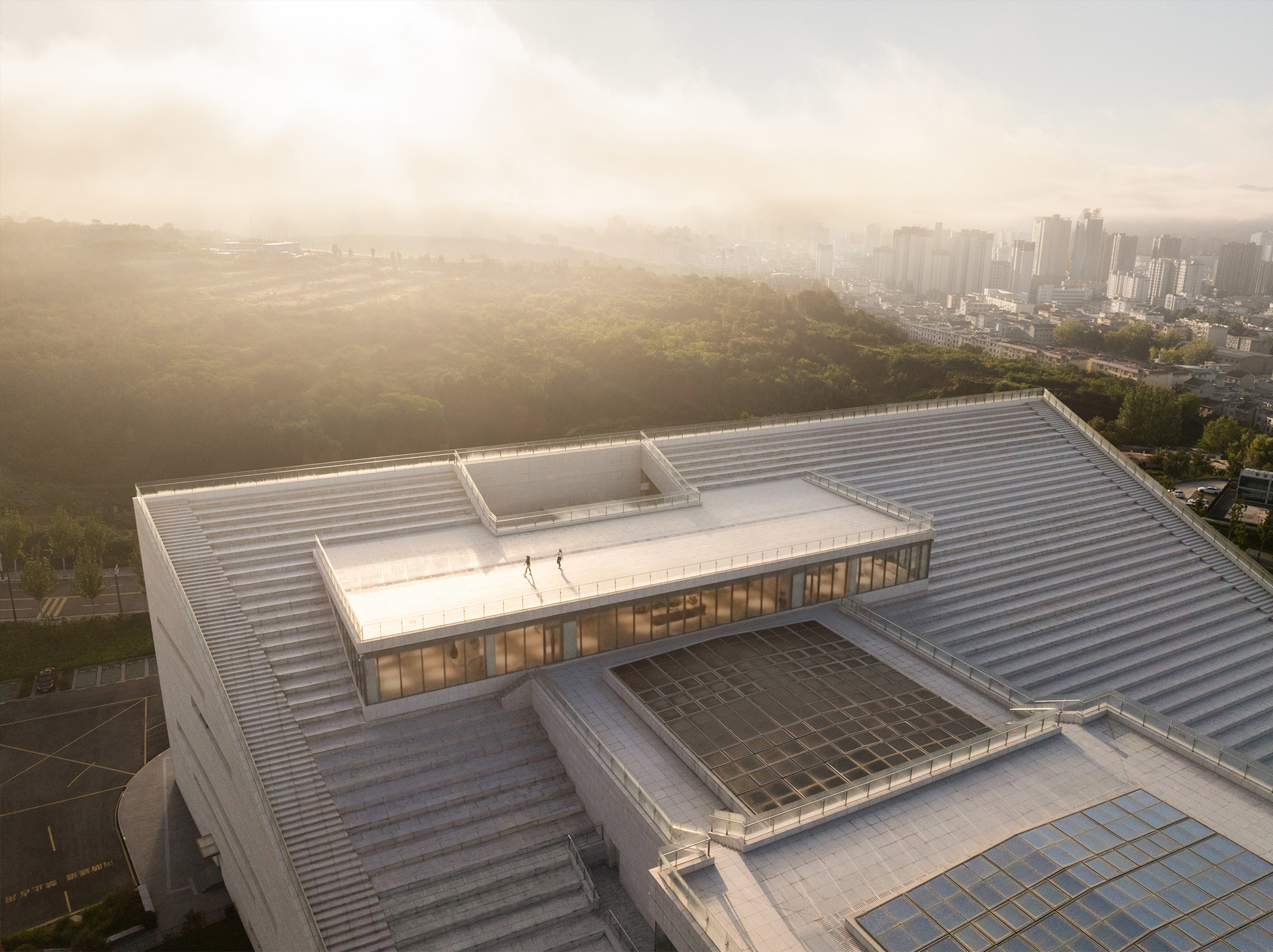 Aerial view of the stepped metal roof terraces with skylights overlooking a hazy valley