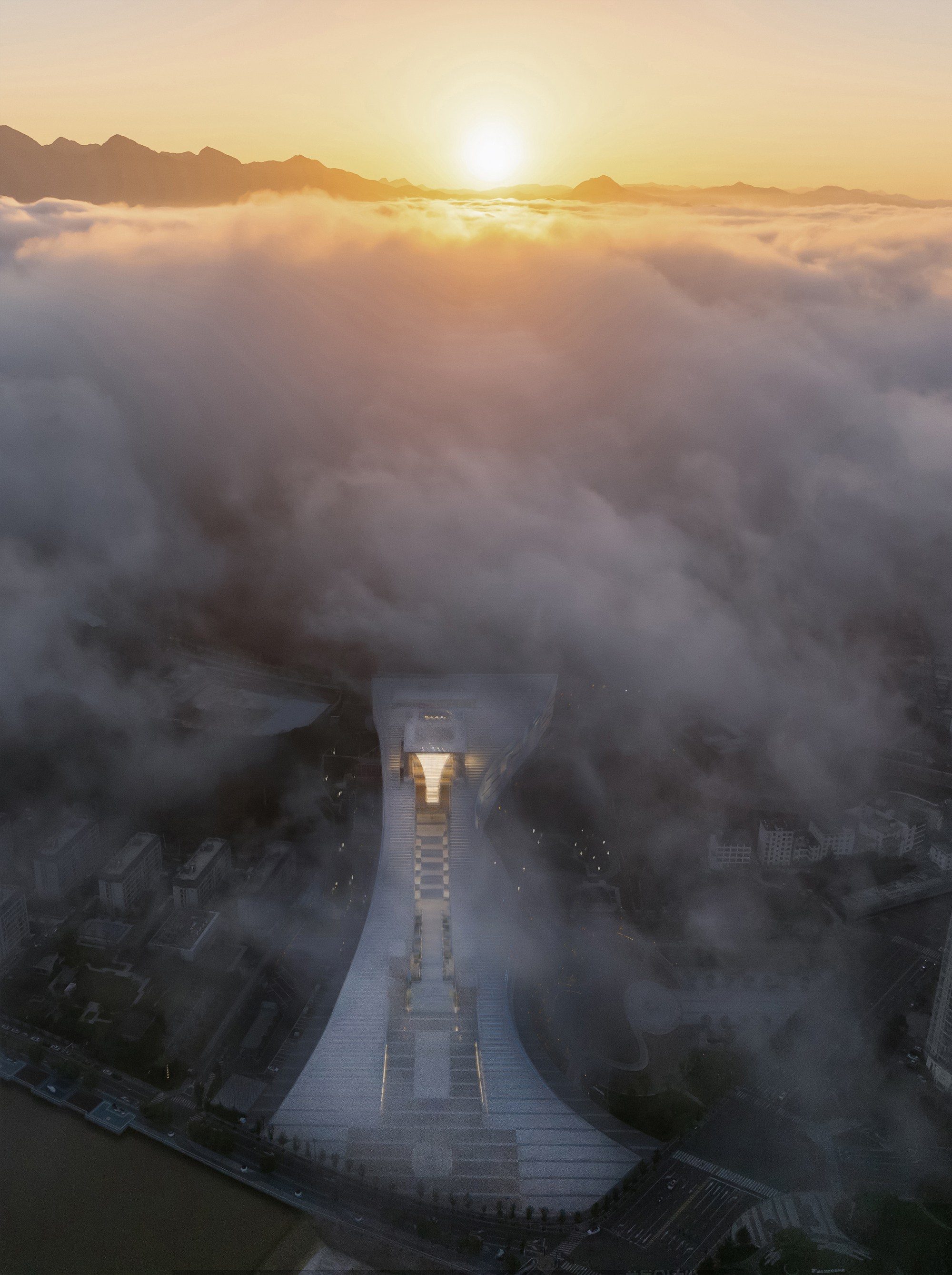 Aerial view of the illuminated monumental plaza and central structure emerging from dense morning fog